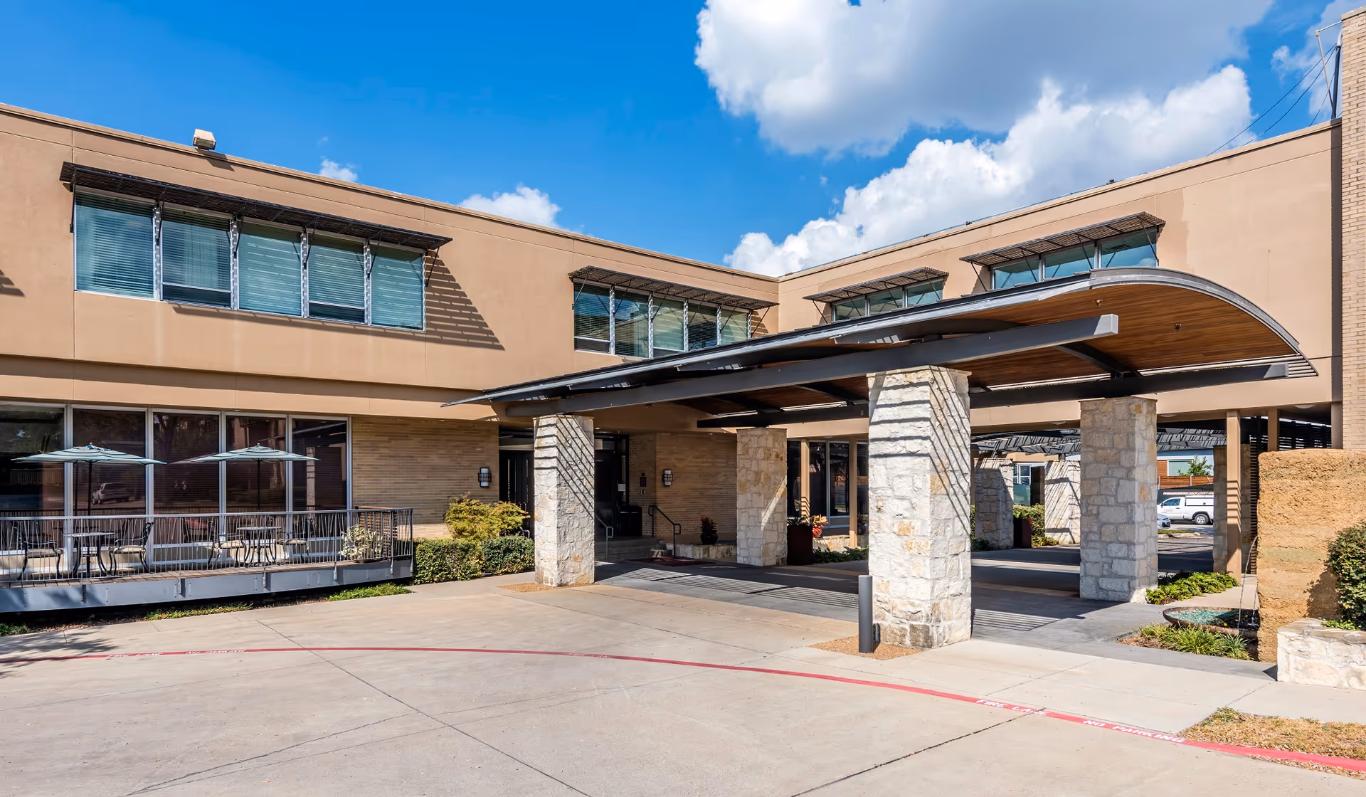 Entrance of a senior living facility with a covered drop-off area and stone pillars.