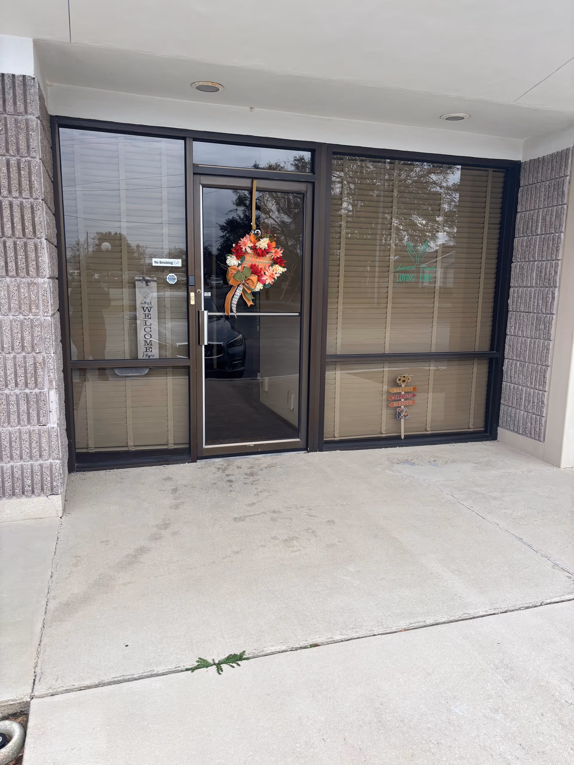 Facility entrance with glass doors, wreath, and window signage under a covered doorway.