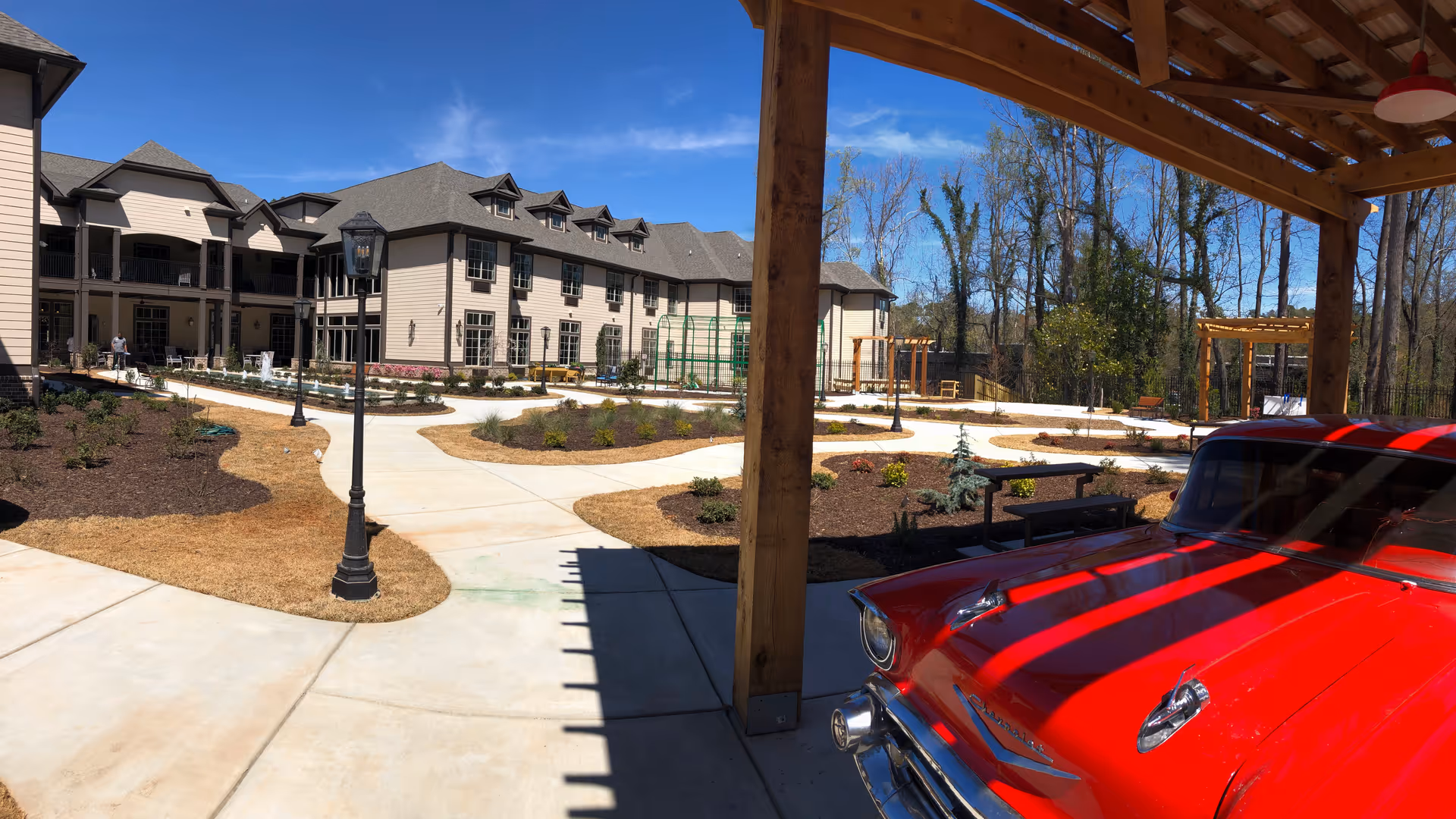Outdoor Orchard Senior Living courtyard with pathways, lampposts, planters, and a red vintage car.