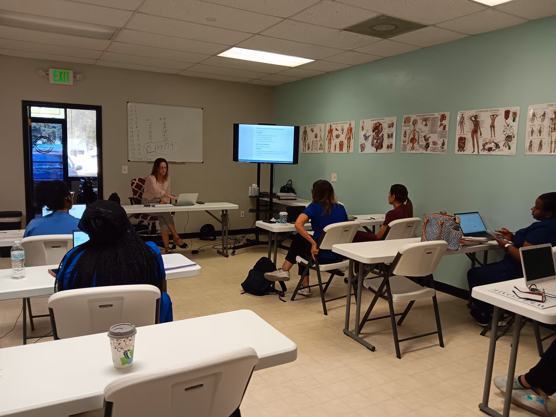 Instructor leads a training session in a classroom with trainees using laptops.