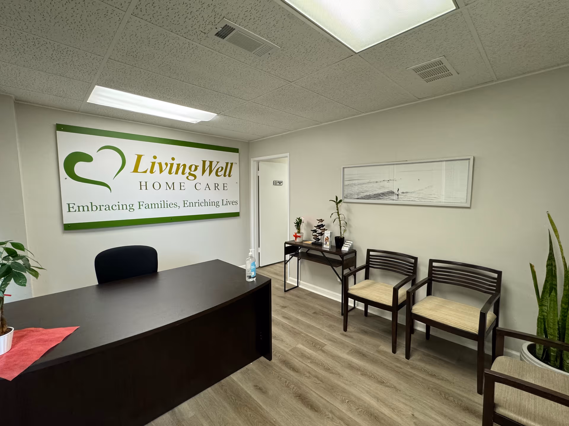 Reception area featuring a dark desk, wall sign, chairs, plants, and decorative accents.