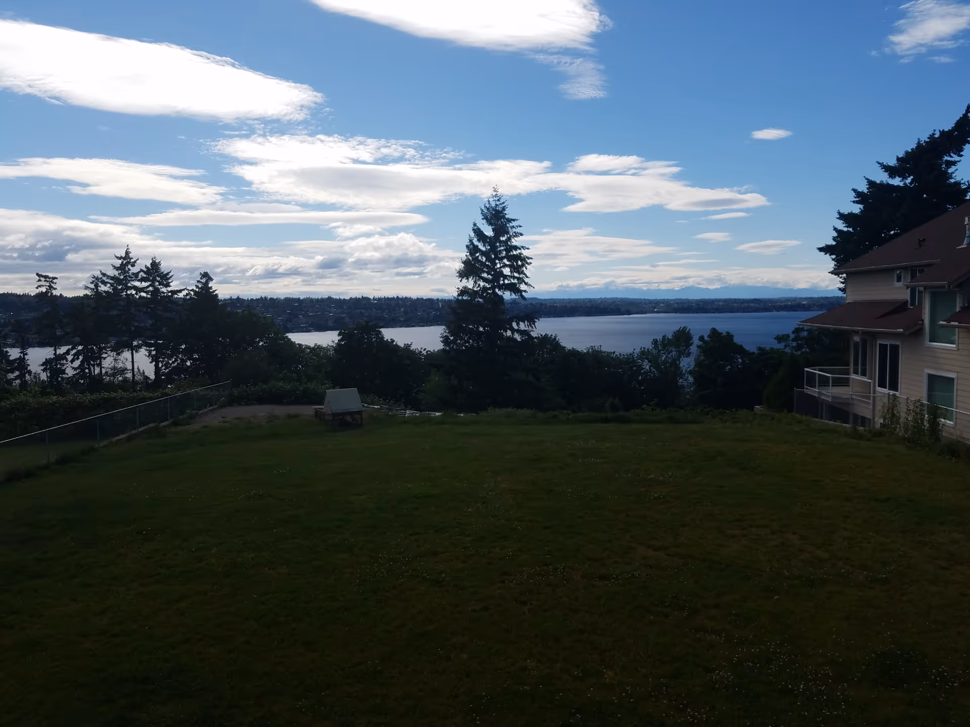 Open grassy yard with a scenic lake view, trees, and a neighboring building.