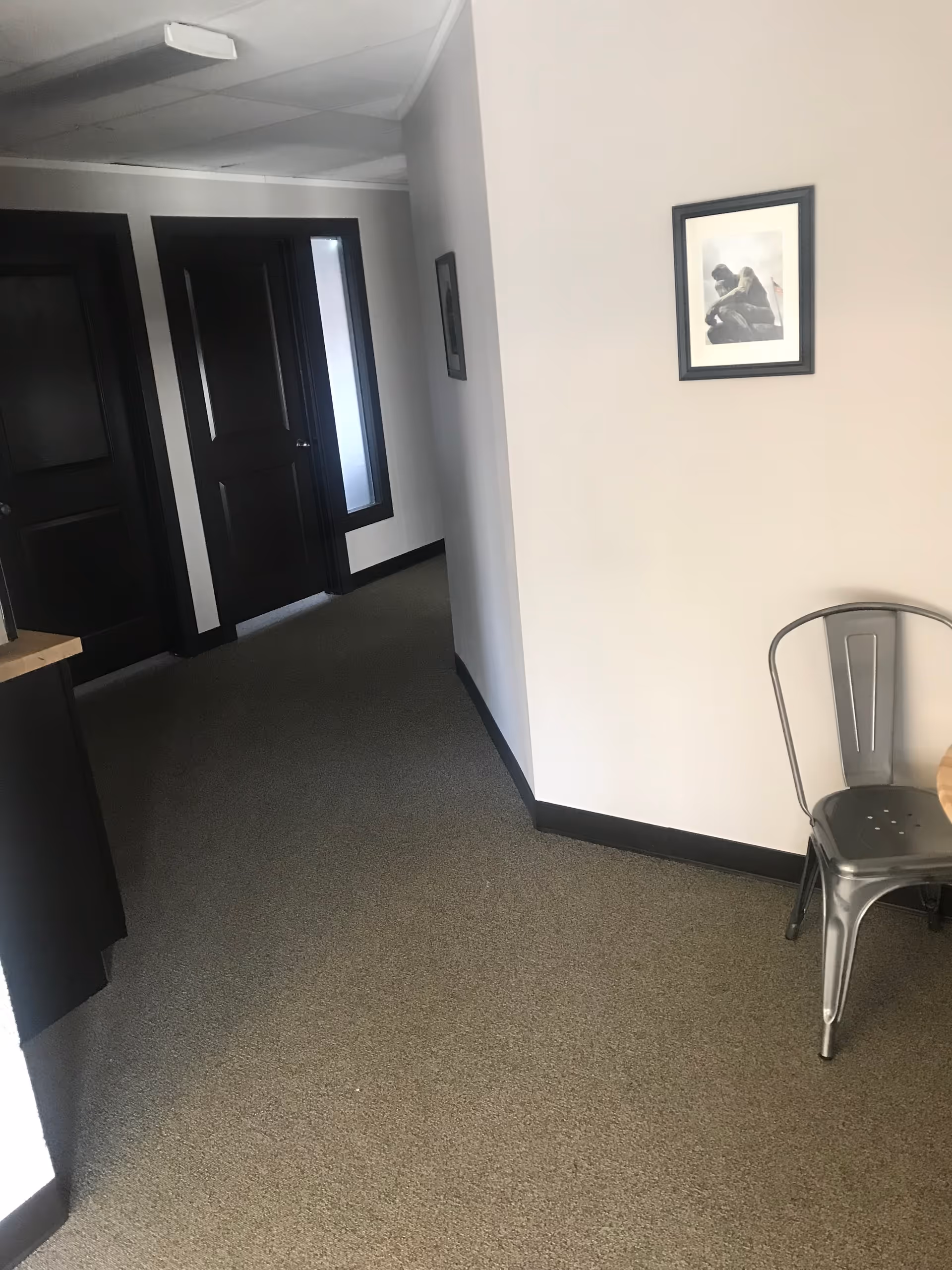 Narrow hallway inside a senior living facility with doors, framed pictures, and a metal chair.