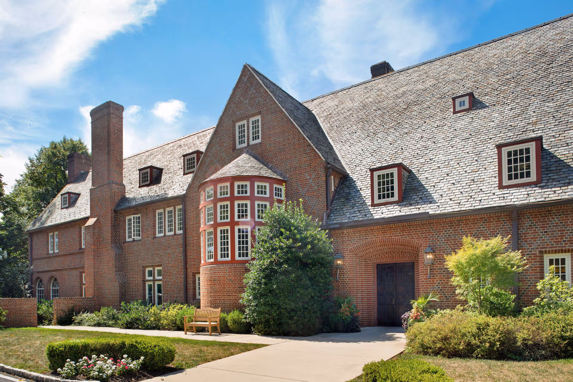 Brick senior living building exterior featuring a curved bay window, sloped roof, and landscaped grounds.