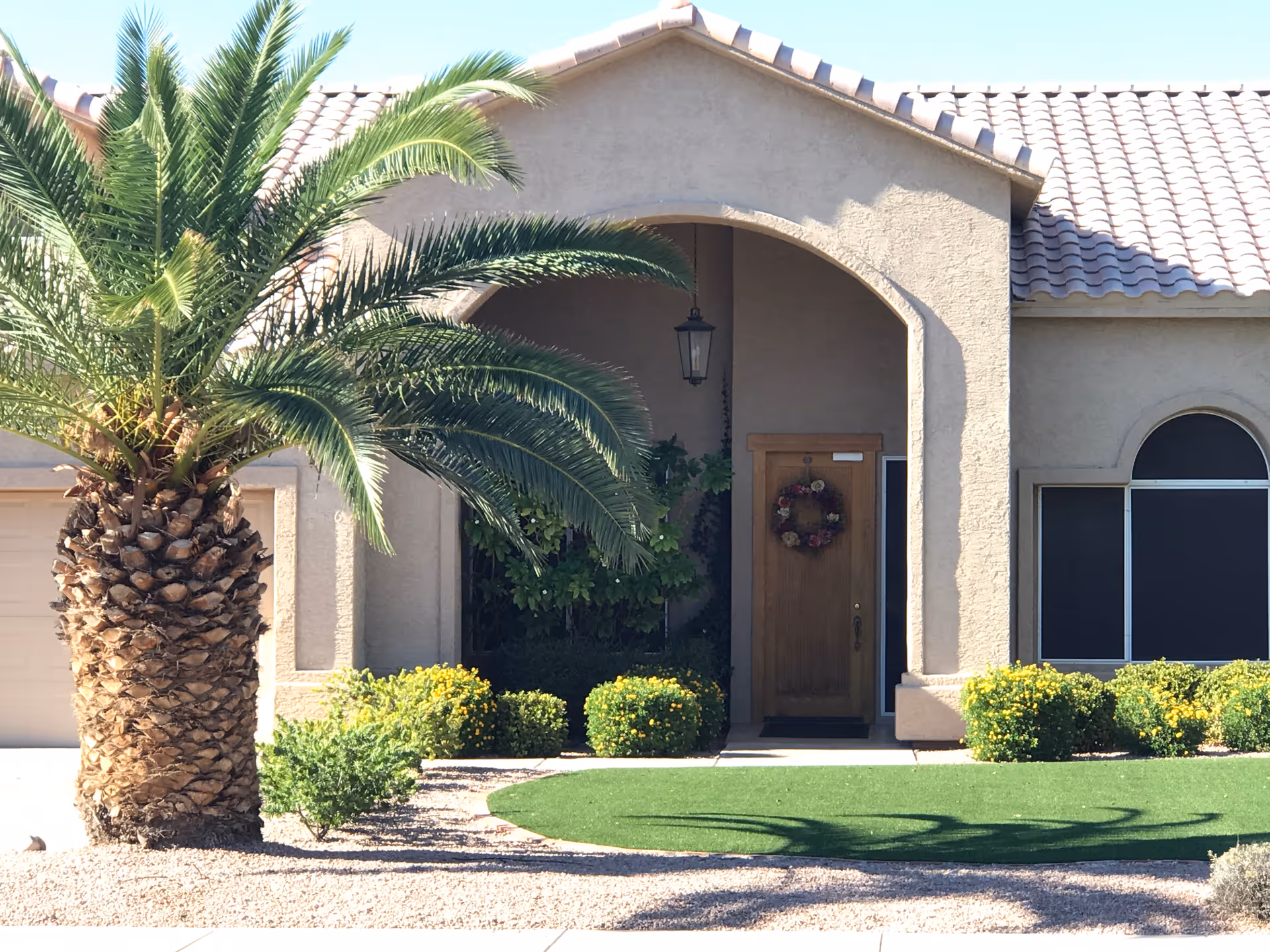 Front entrance of a beige stucco house with palm tree and landscaping