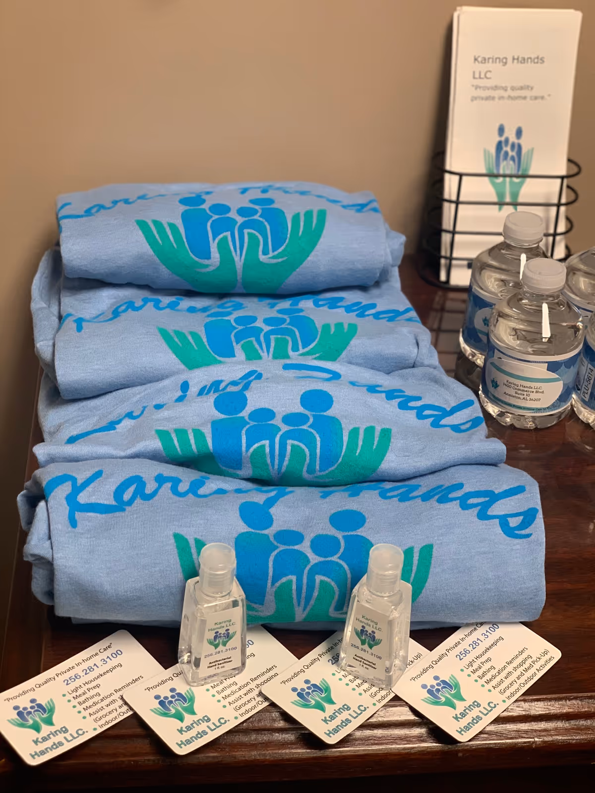 Branded blue towels showing Karing Hands LLC, with sanitizer bottles and brochures on a wooden counter.