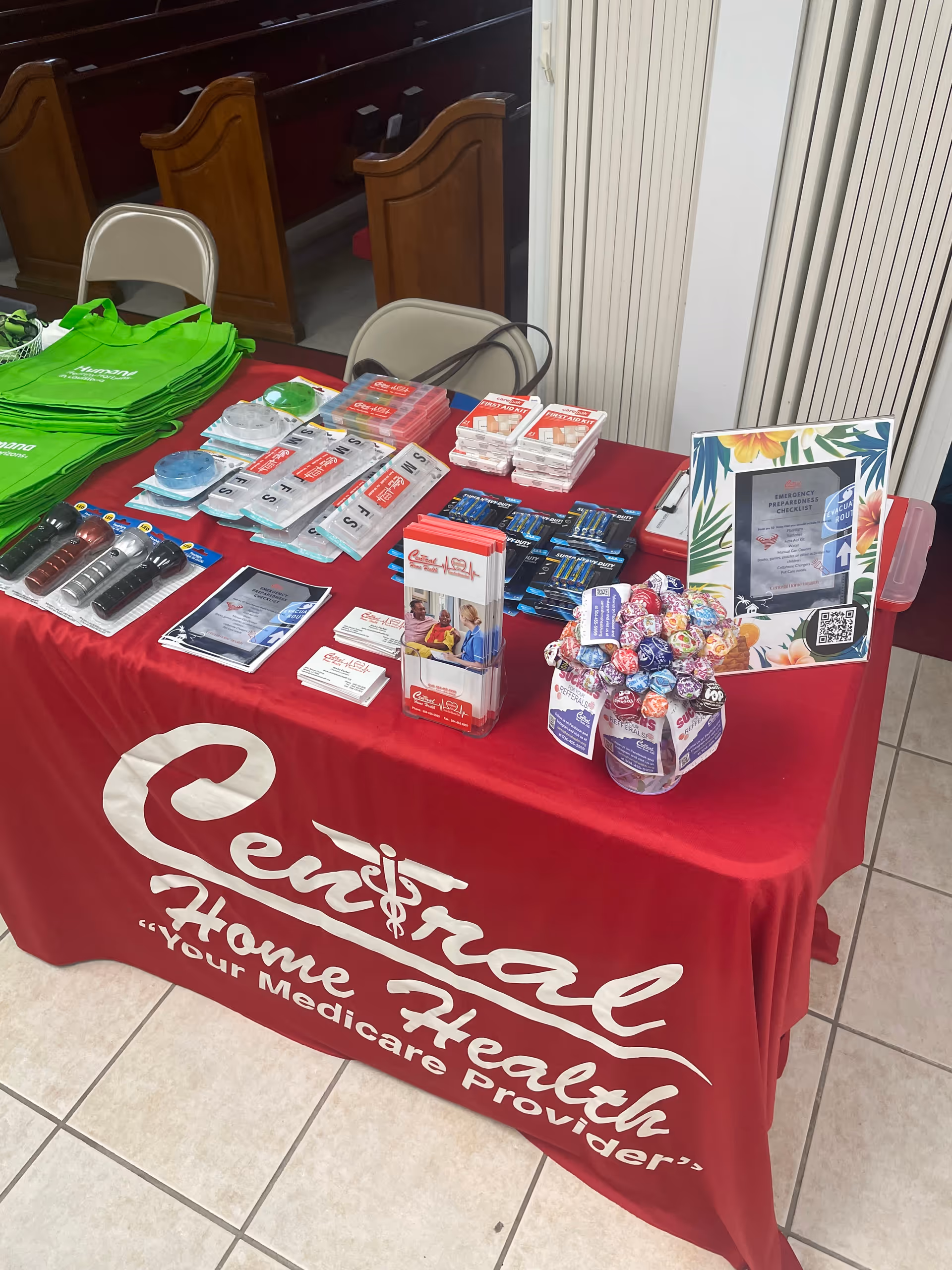 Indoor table displaying promotional materials, health products, and green tote bags on a red cloth.