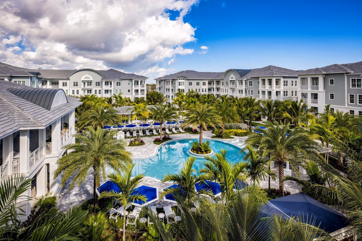 A resort-style senior living campus with a central pool, palm trees, and surrounding buildings.