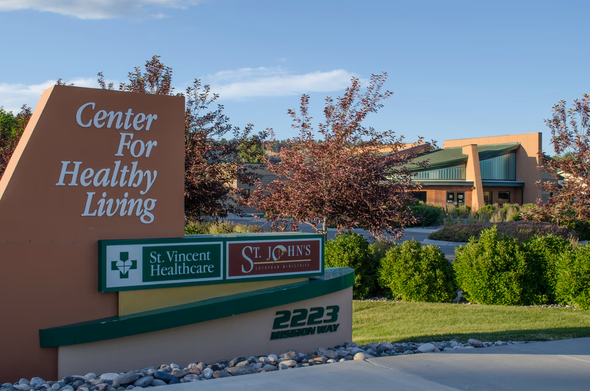 Entrance sign reading 'Center For Healthy Living' and 'St. John's' with landscaped bushes and the facility building in the background.