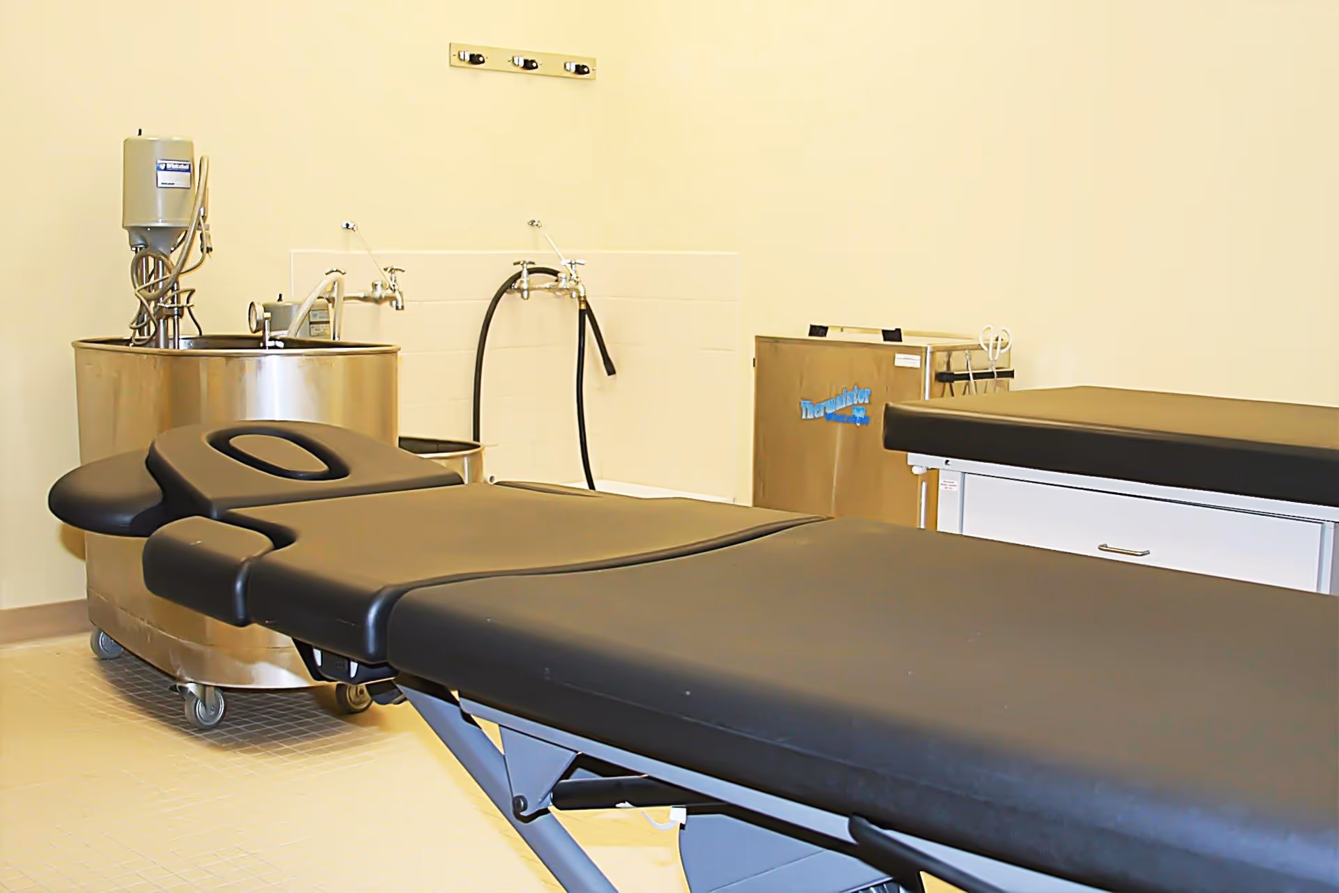 Sterile treatment room with black padded examination table and medical equipment.