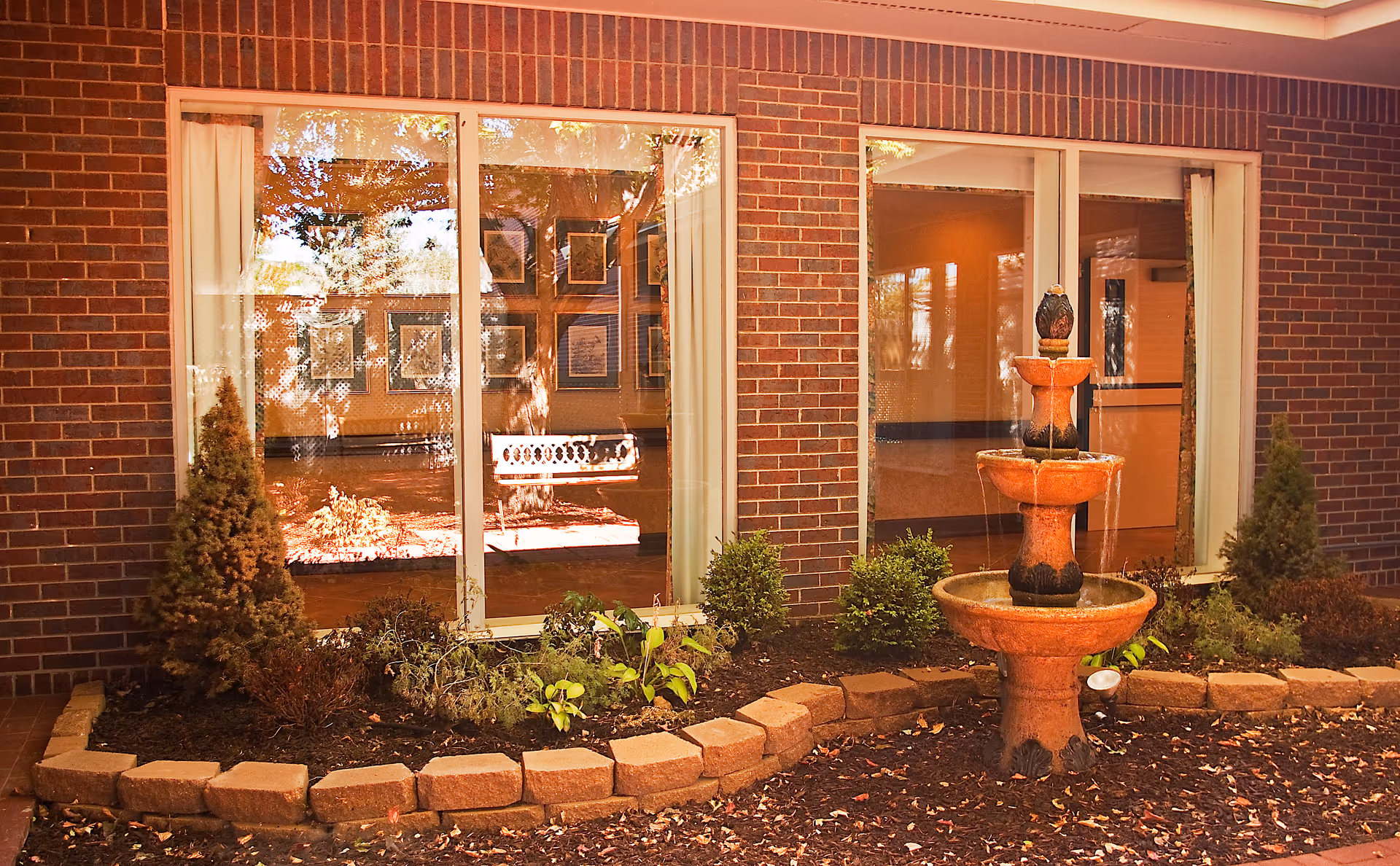 Brick exterior of Orchard Park Health Care Center with a stone fountain and garden beds.