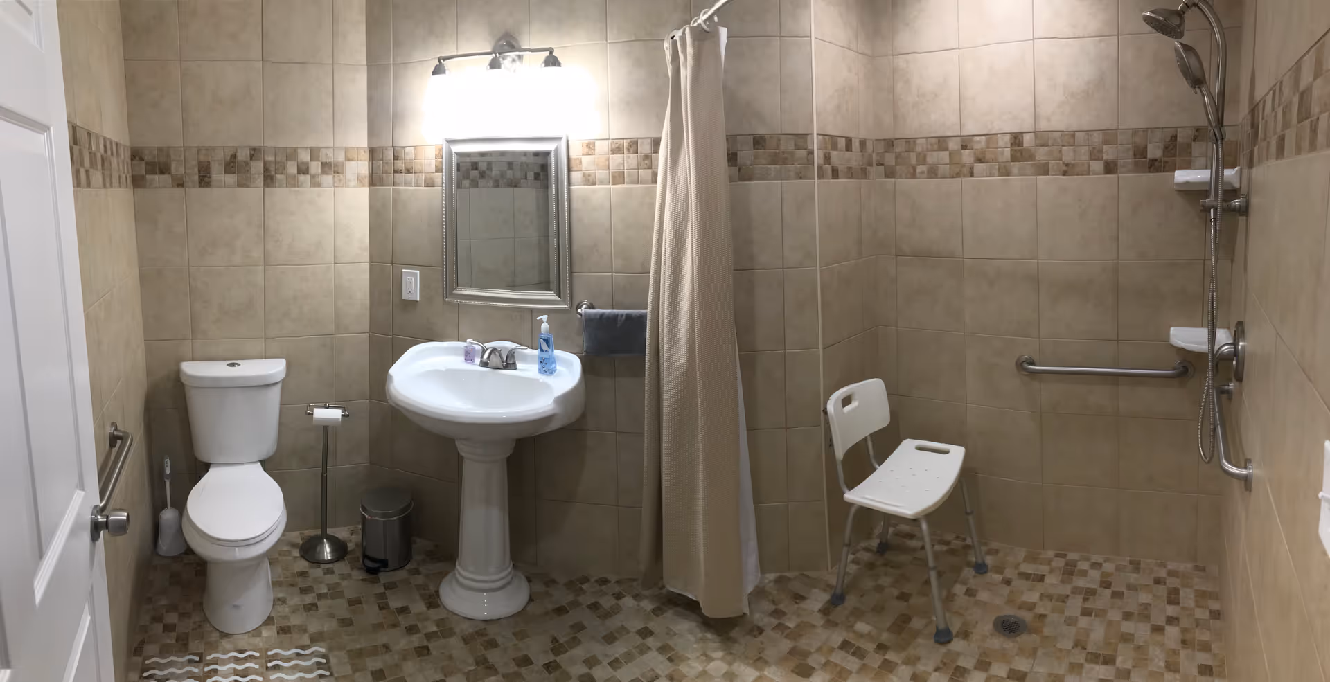 Accessible bathroom with toilet, pedestal sink, shower, curtain, and grab bars.