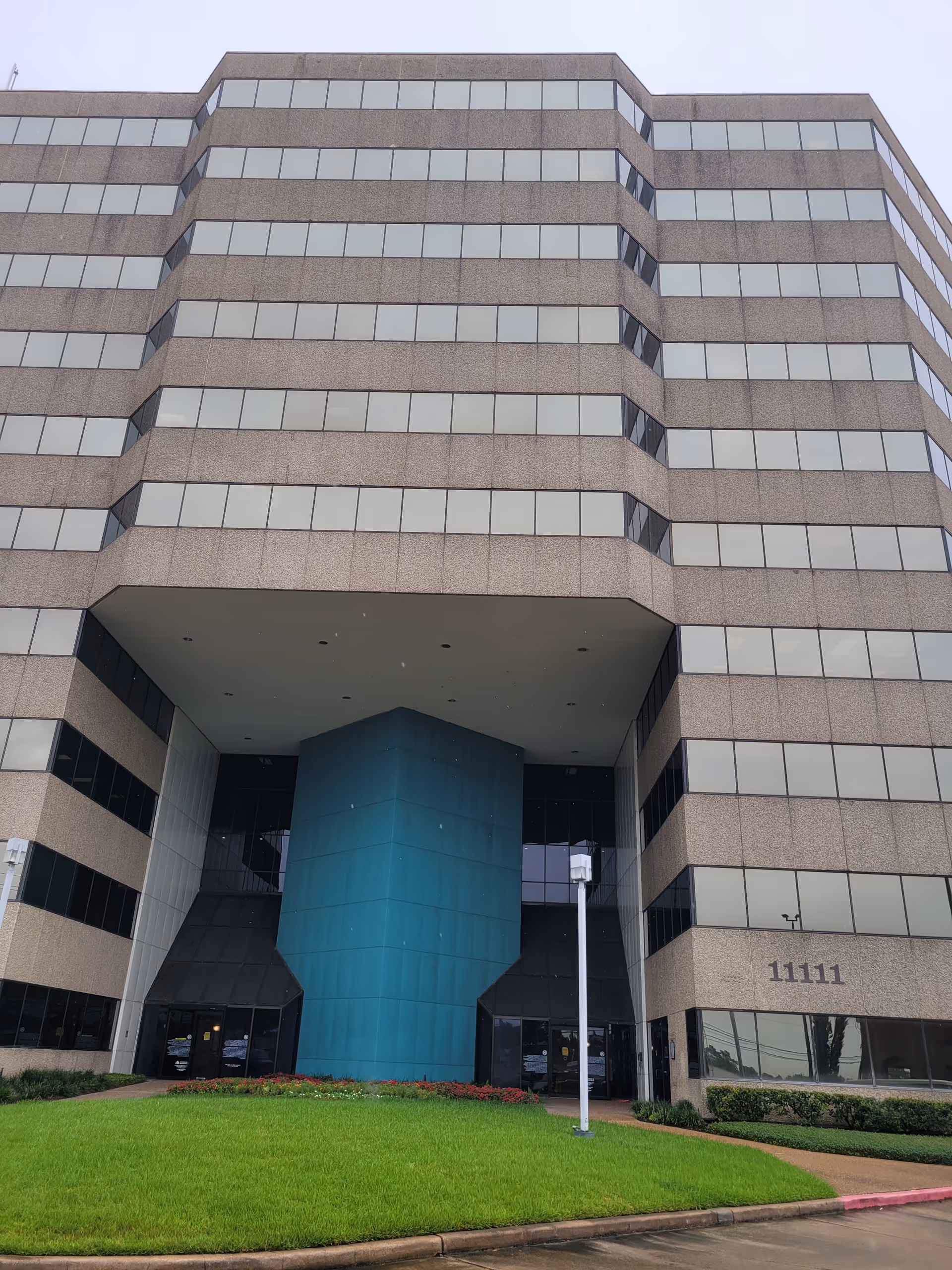 Tall beige office-style building with a bright blue entrance pillar and manicured lawn.