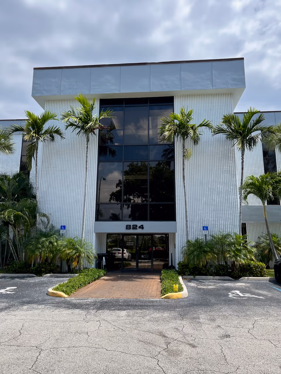 Modern white facility exterior with large glass entry and palm trees.