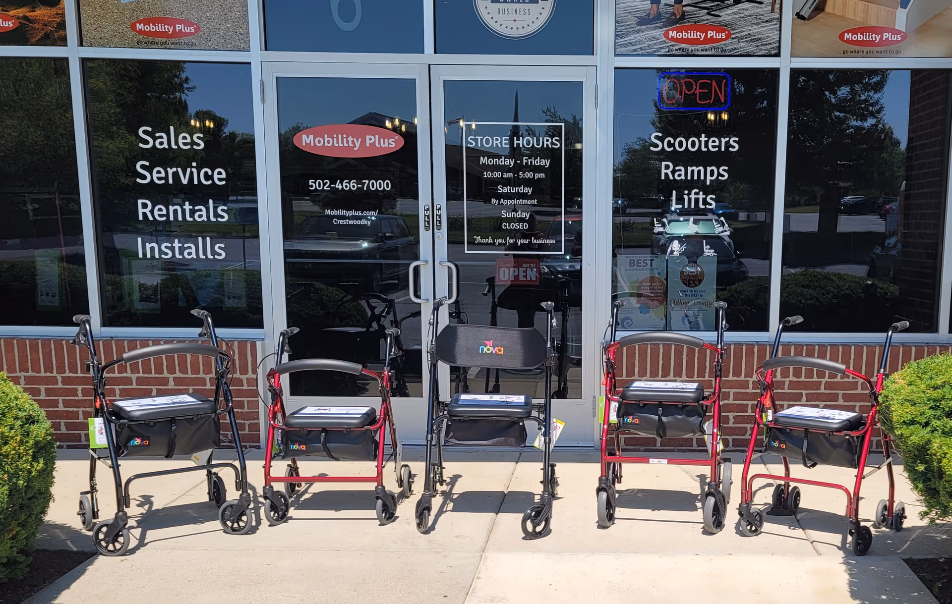 Row of mobility scooters lined up outside Mobility Plus storefront with signs.