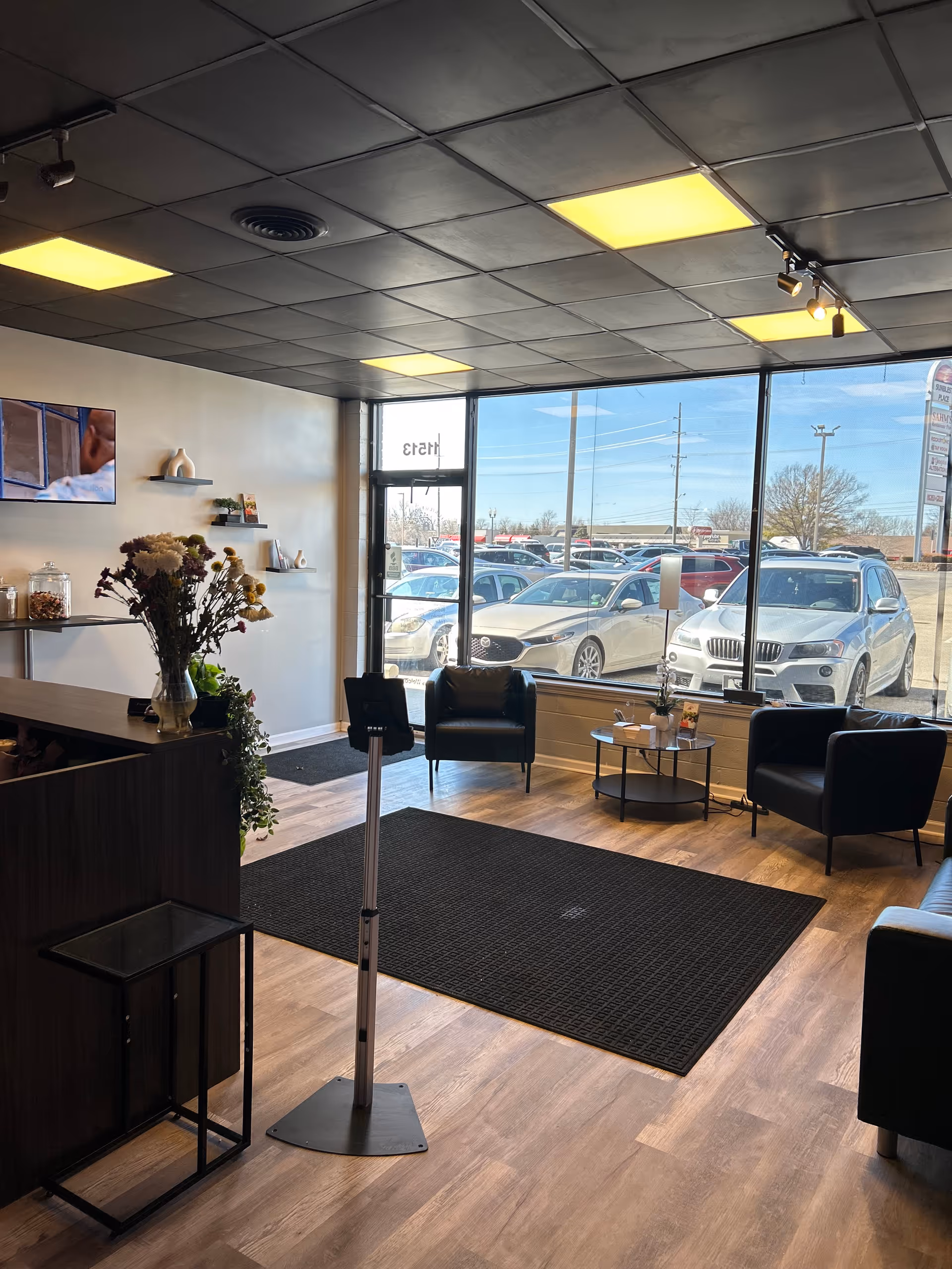 Lobby area with black chairs, a rug, flowers, and large front windows.