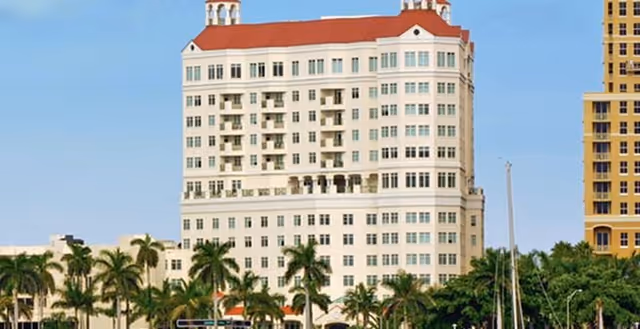 White multi-story senior living building with red roof and palm trees in foreground