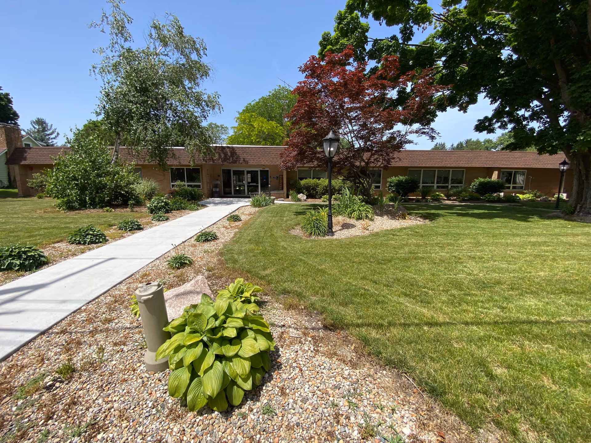Exterior of a single-story senior living center with a walkway, lawn, and trees.