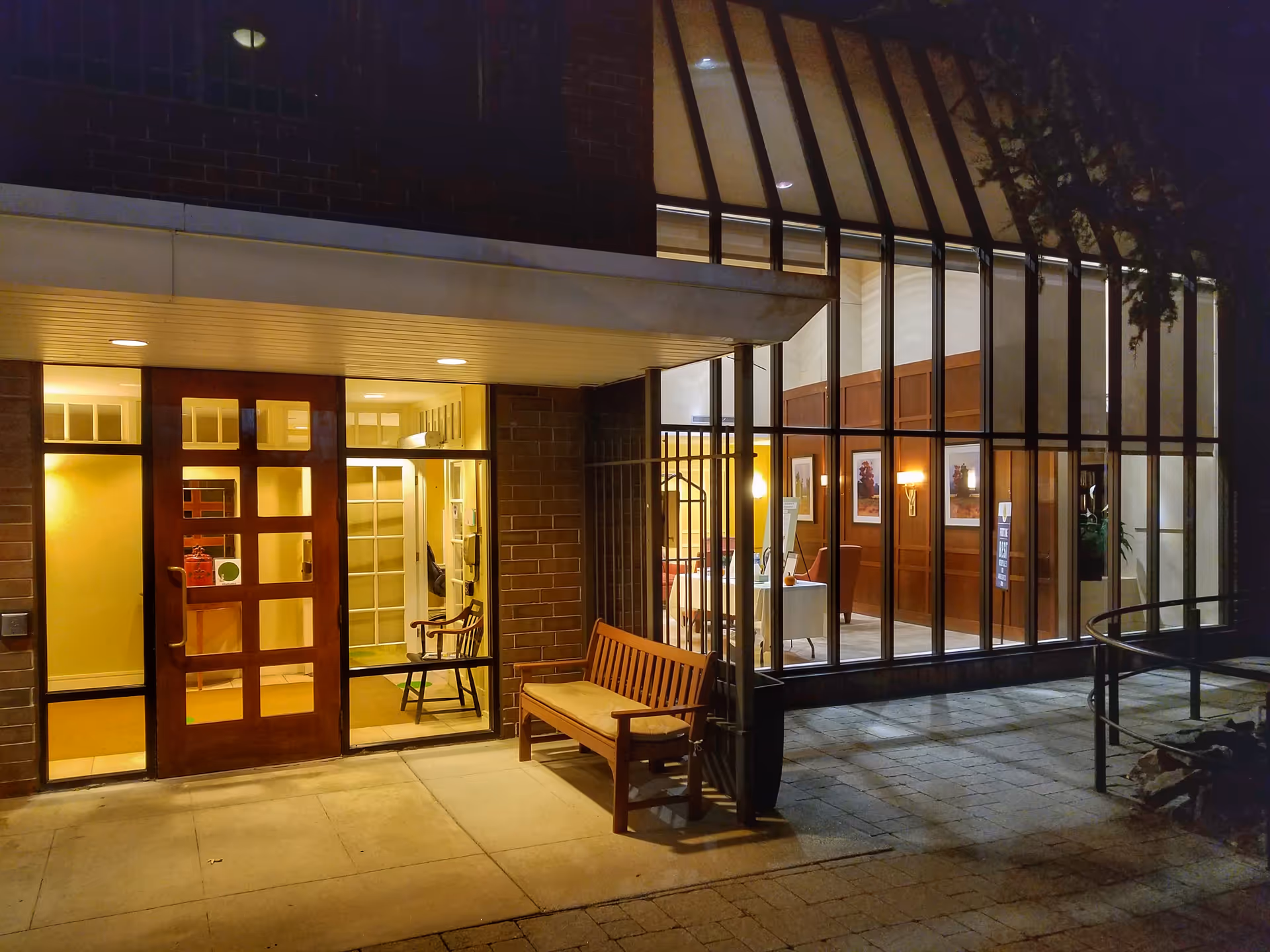 Night exterior view of AVIVA Country Club Heights entrance with glass storefront and bench