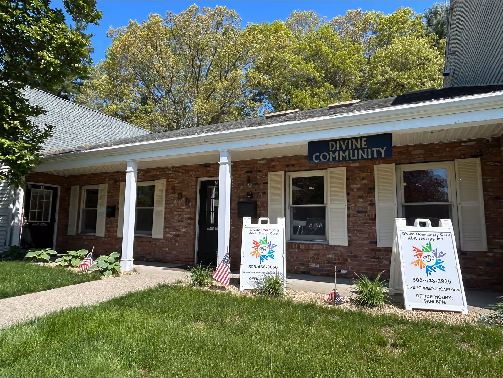 Brick building with a covered front porch labeled Divine Community, signs and American flags outside.