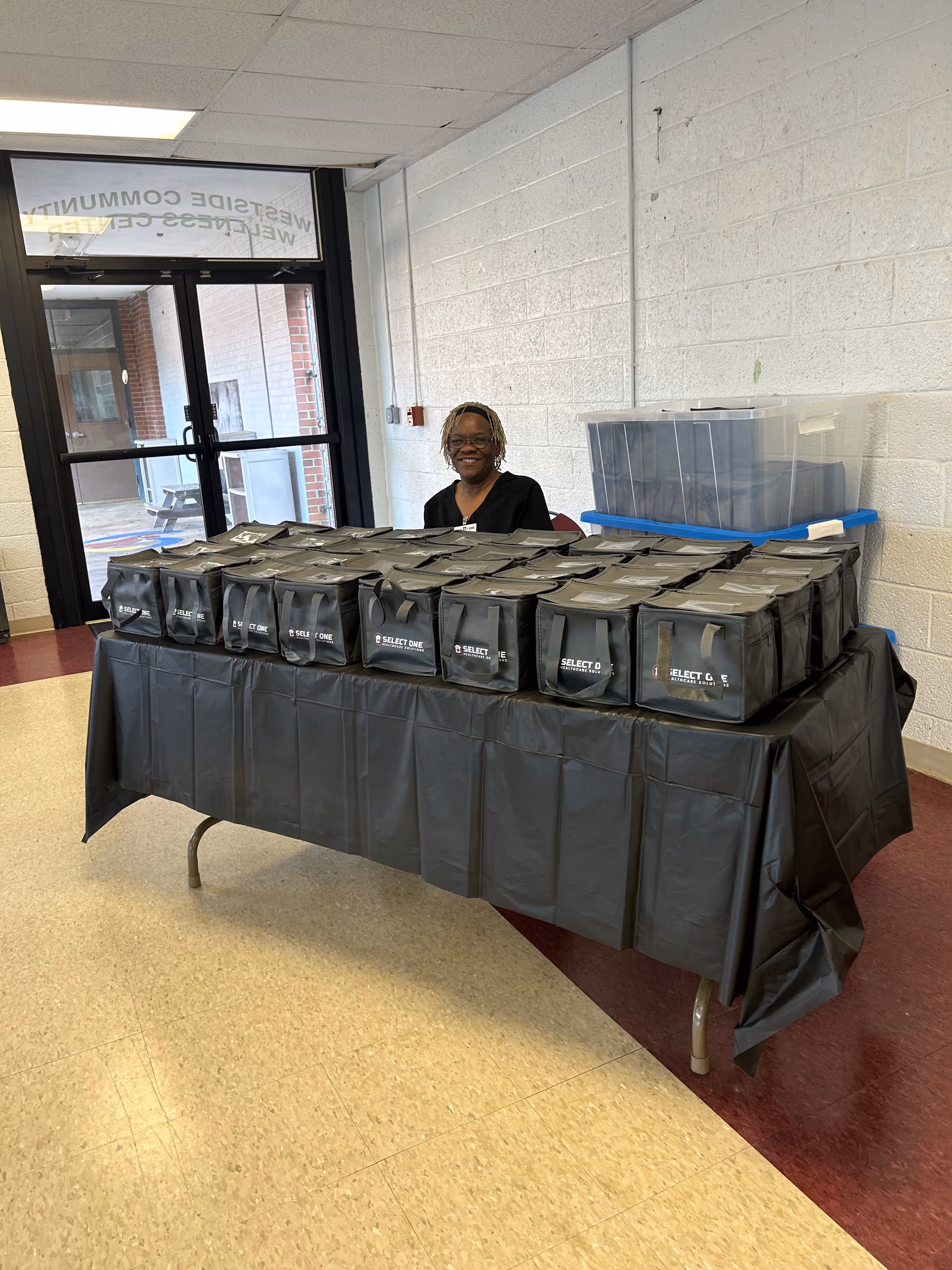 A staff member sits behind a table of many black gift bags inside a facility.