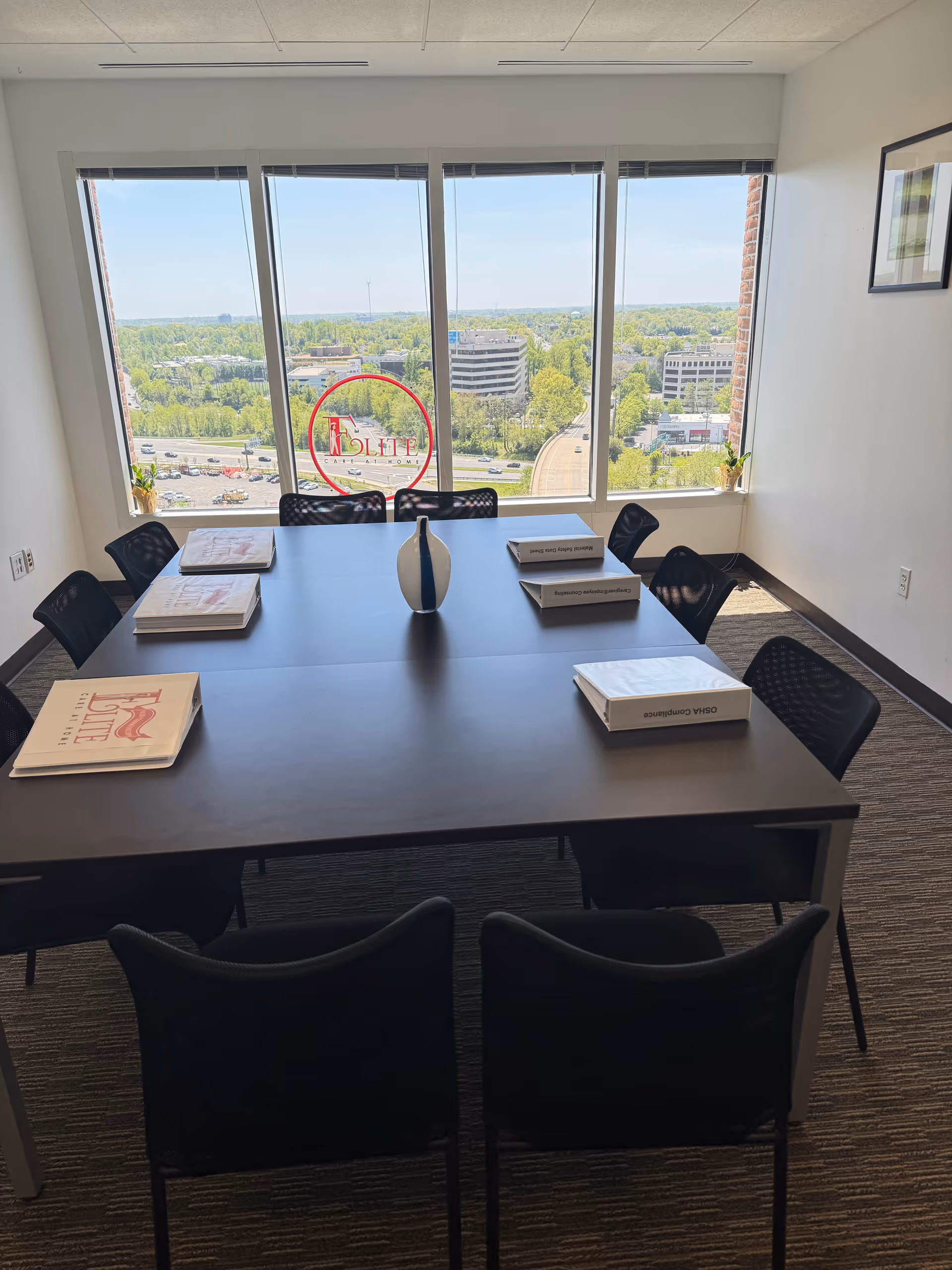 Conference room with large table, black chairs, and Elite logo on windows overlooking cityscape.
