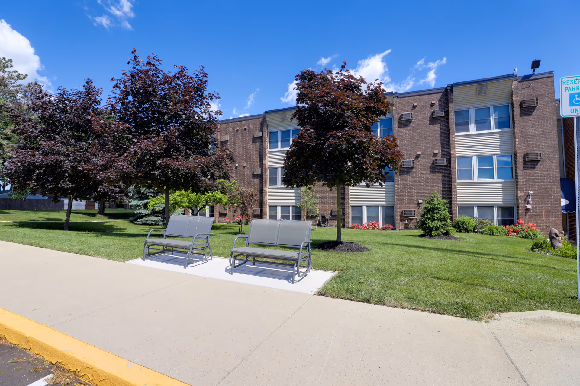 The Bellaire Senior Living building exterior with trees, lawn, and benches along the sidewalk.
