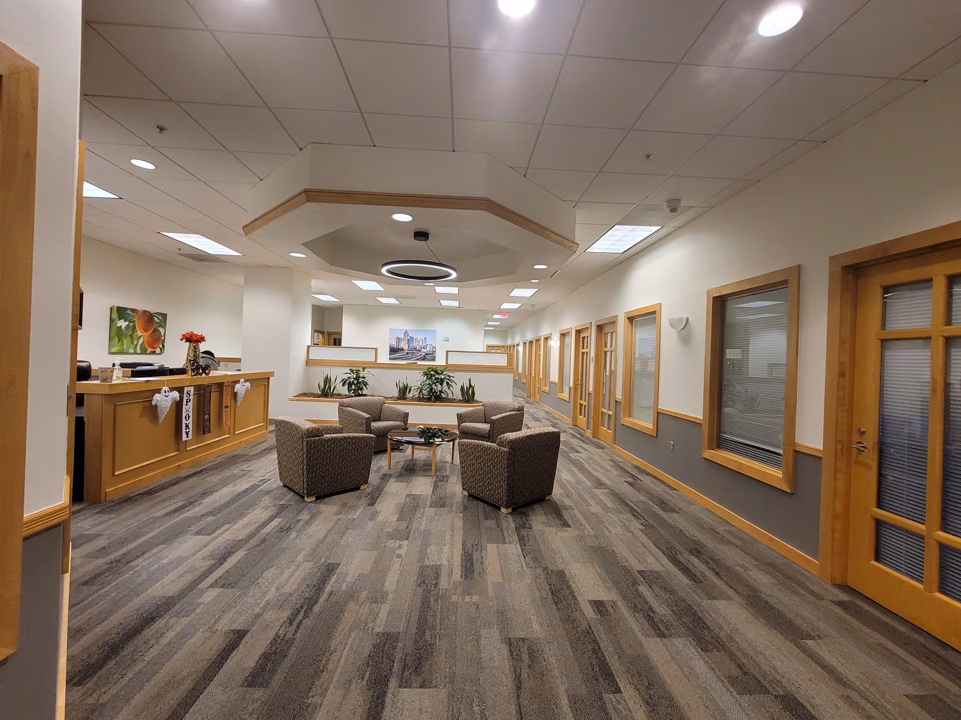 Empty indoor senior living lobby with seating area, reception desk, and glass doors along hallway.