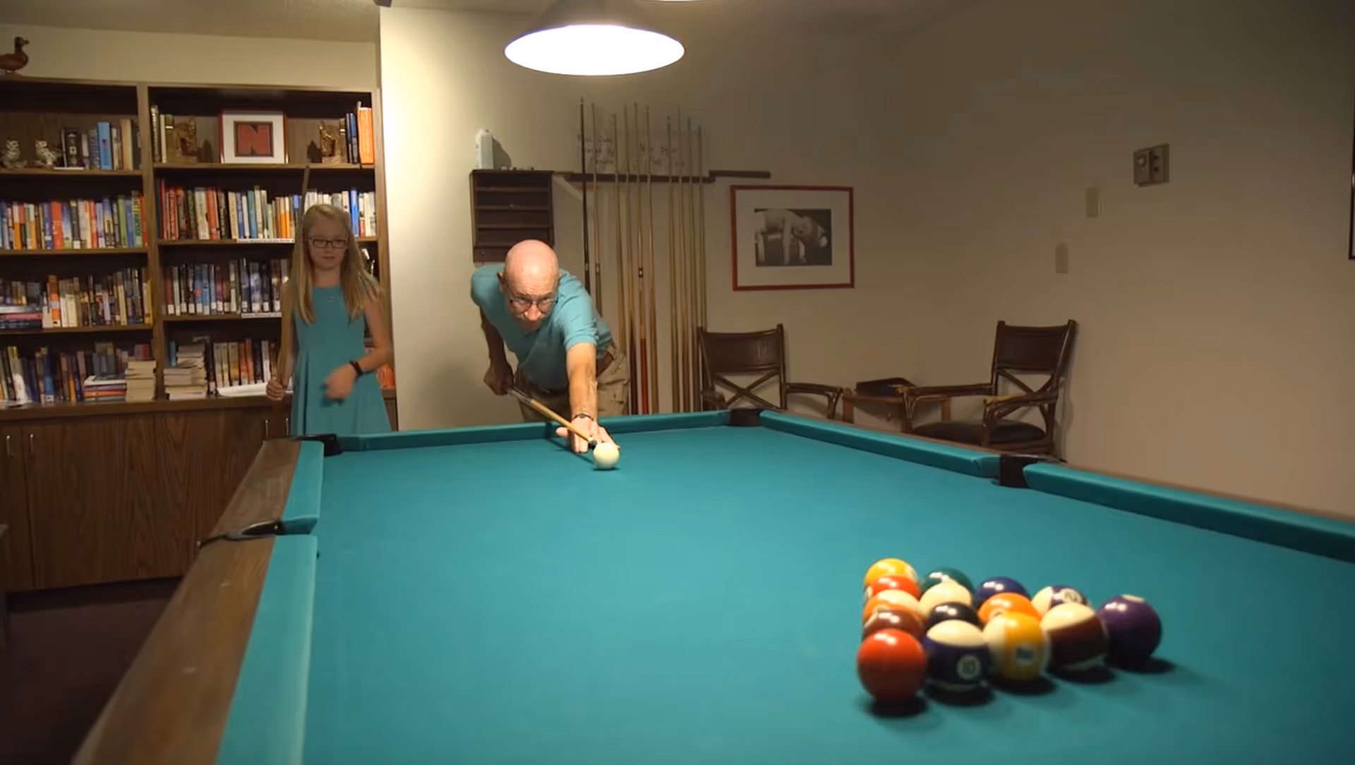 Indoor recreation room with a pool table as two people prepare to shoot.