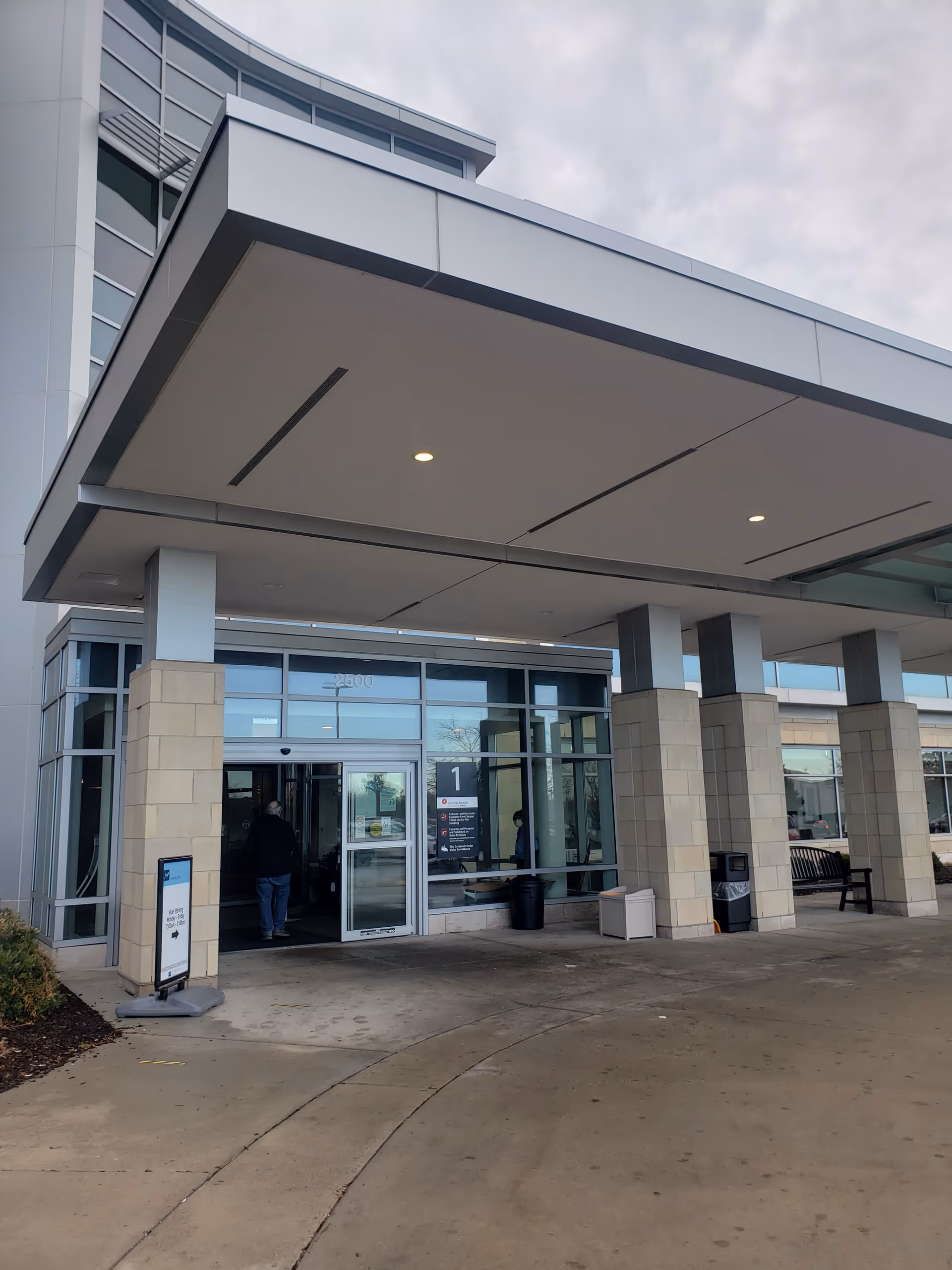 Modern senior living facility entrance with glass doors, pillars, and a covered drop-off area.