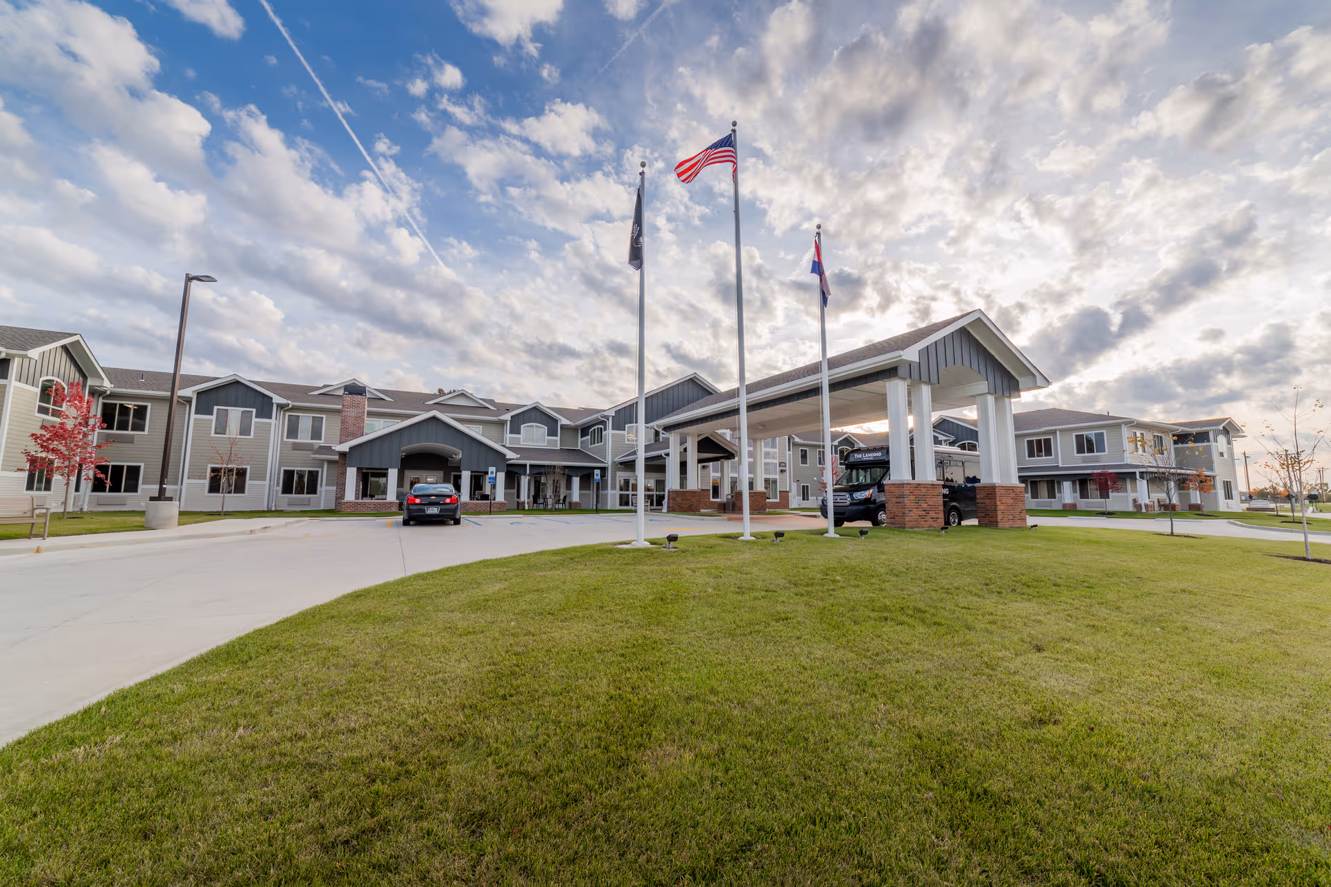 Exterior view of The Landing of O'Fallon with flagpoles, driveway, and well-kept lawn.