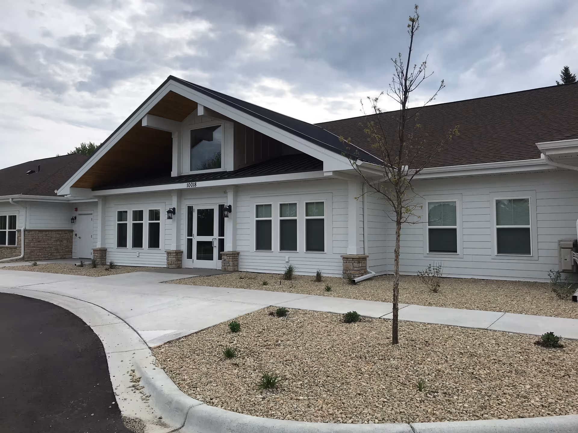 White, single-story senior living facility with a gabled entrance and gravel landscaping.