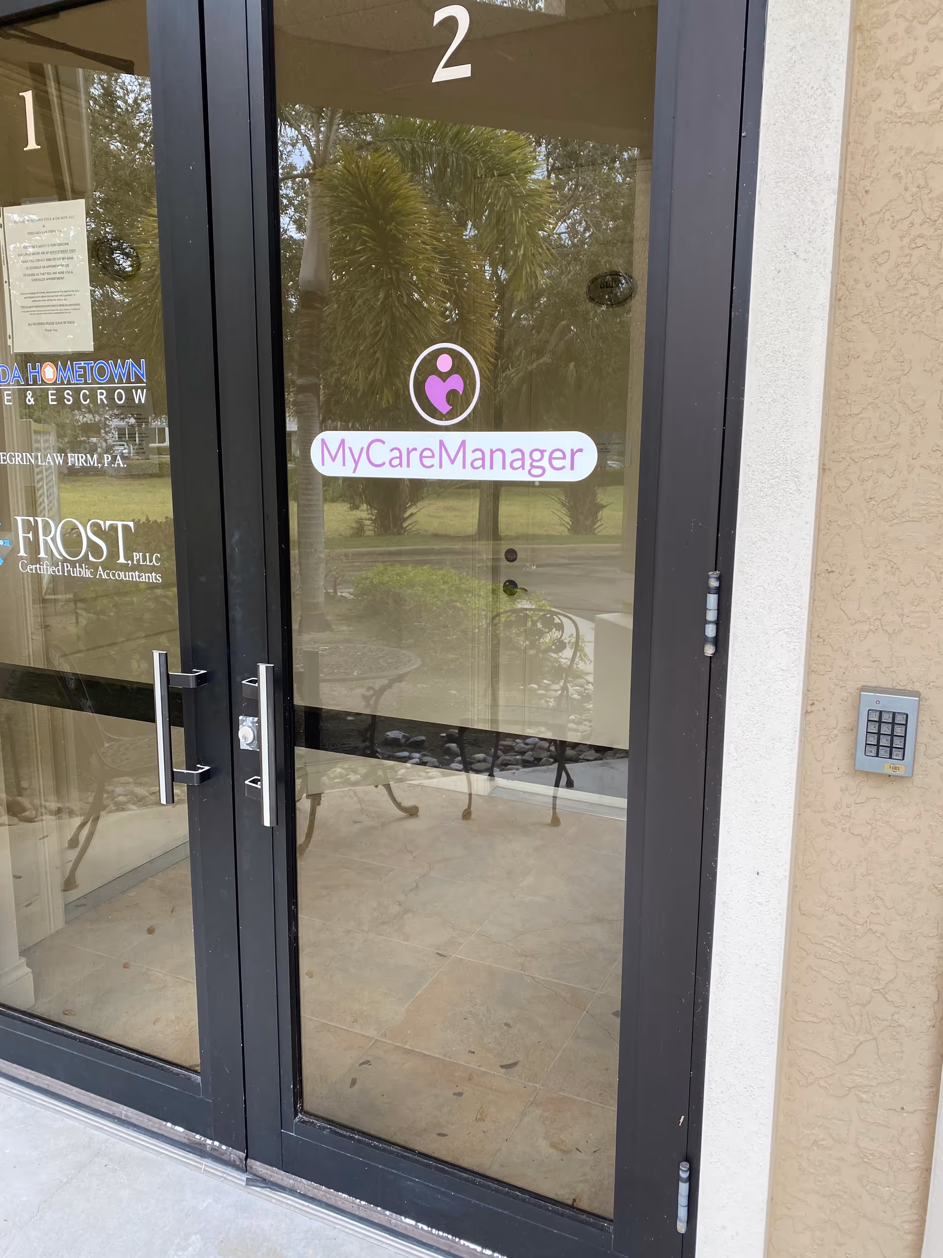 Glass entrance door with MyCareManager sign, reflection of palms, and indoor seating.
