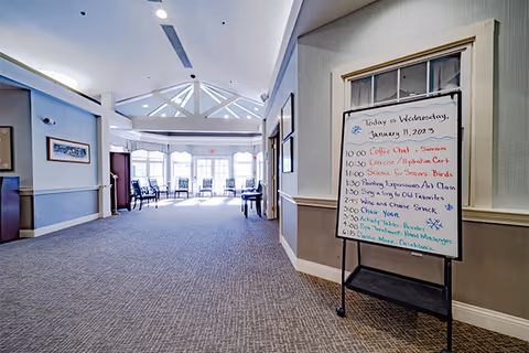 Wide interior hallway of a senior living facility with a whiteboard schedule.