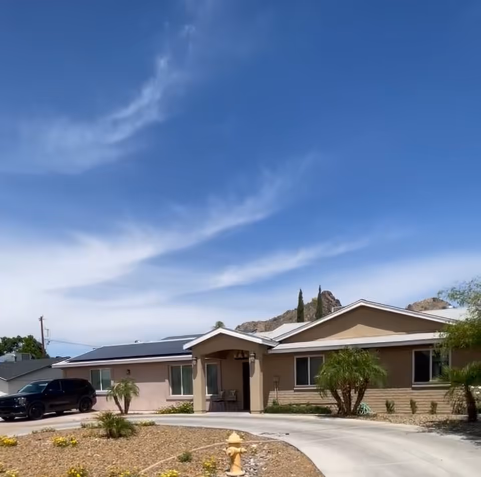 Single-story senior living building with beige facade, driveway, and landscaped front yard.