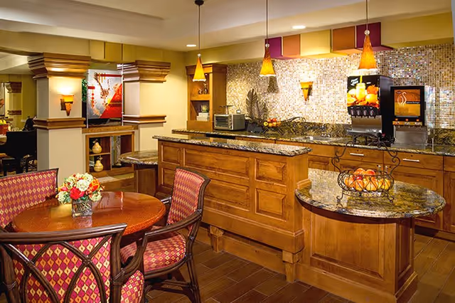 Cozy dining and kitchenette area with a round table and upholstered chairs, wooden cabinetry, granite counters and pendant lights.
