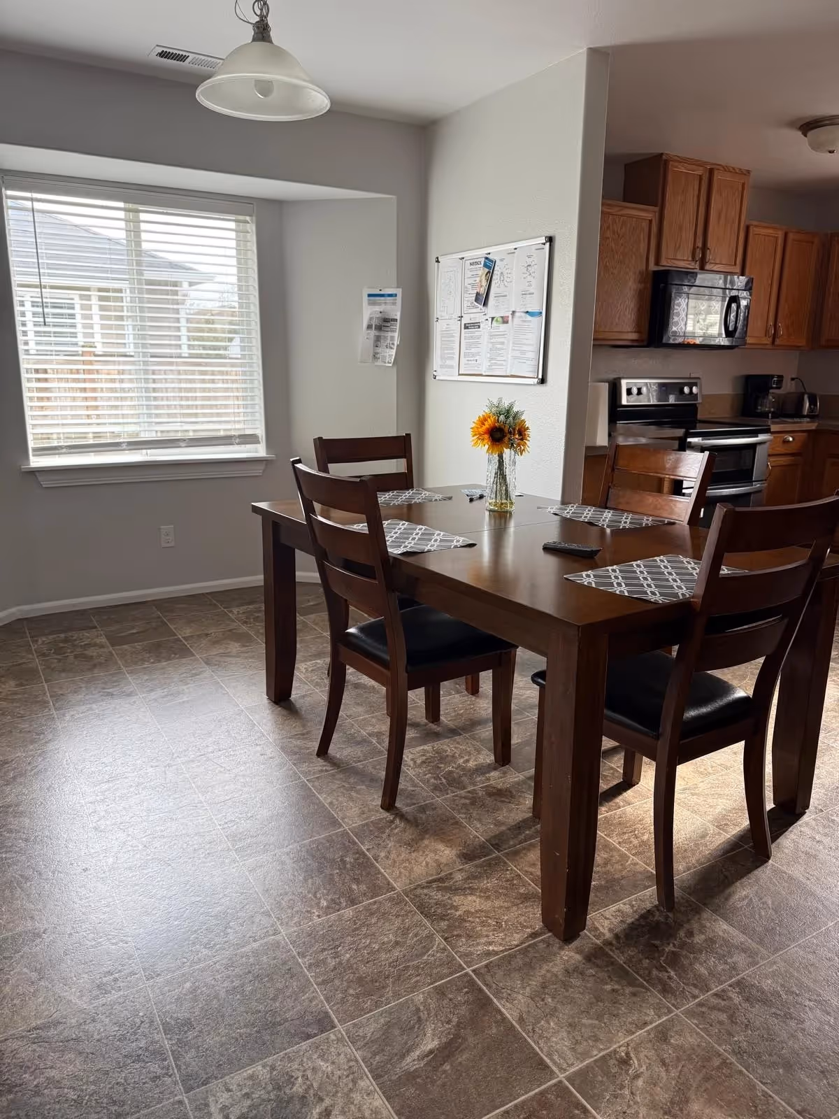 A wooden dining table with six chairs sits in a sunlit dining area beside the kitchen.