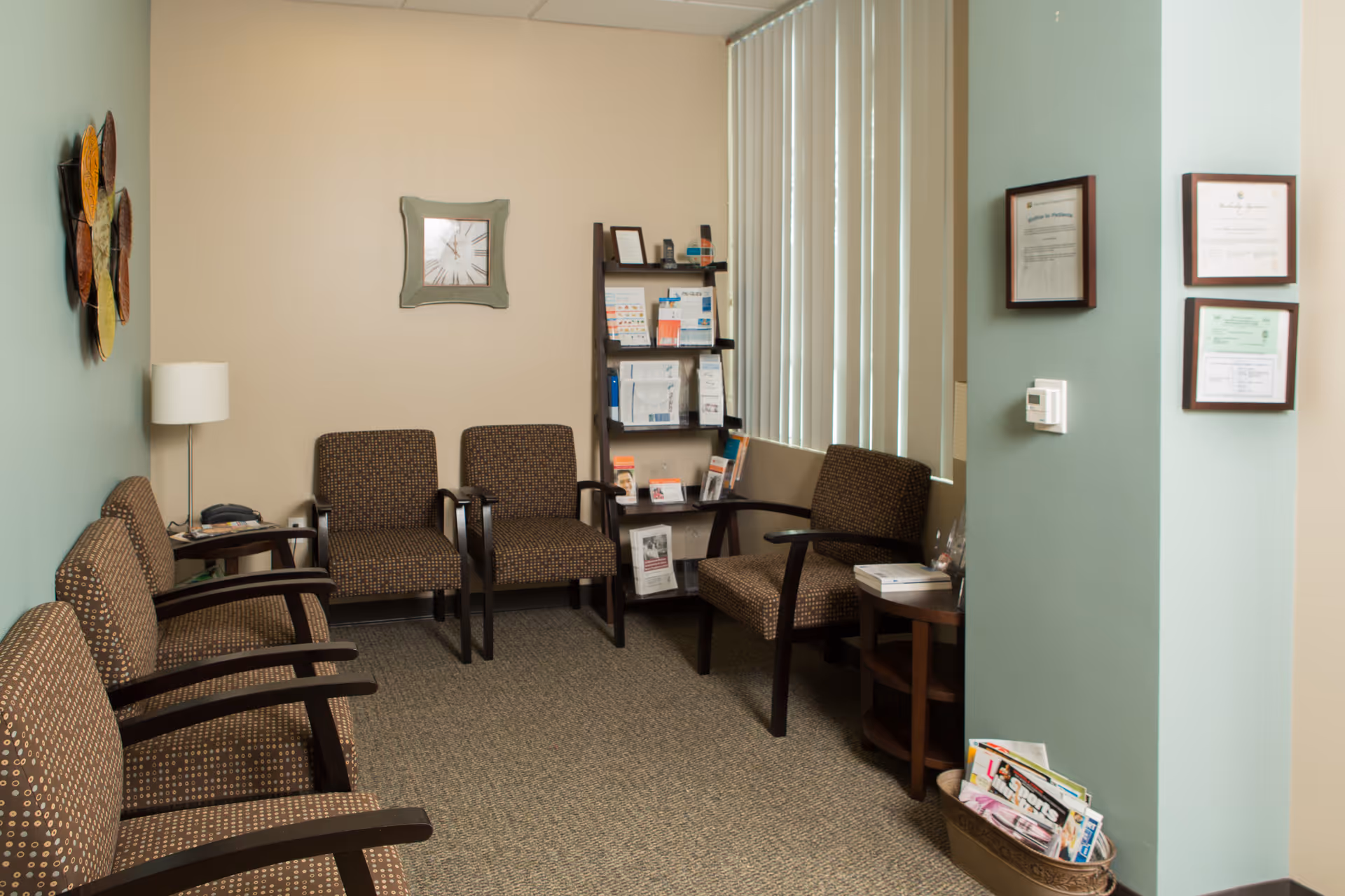 Waiting area with multiple brown chairs, side table, bookshelf, and magazines in a medical office.