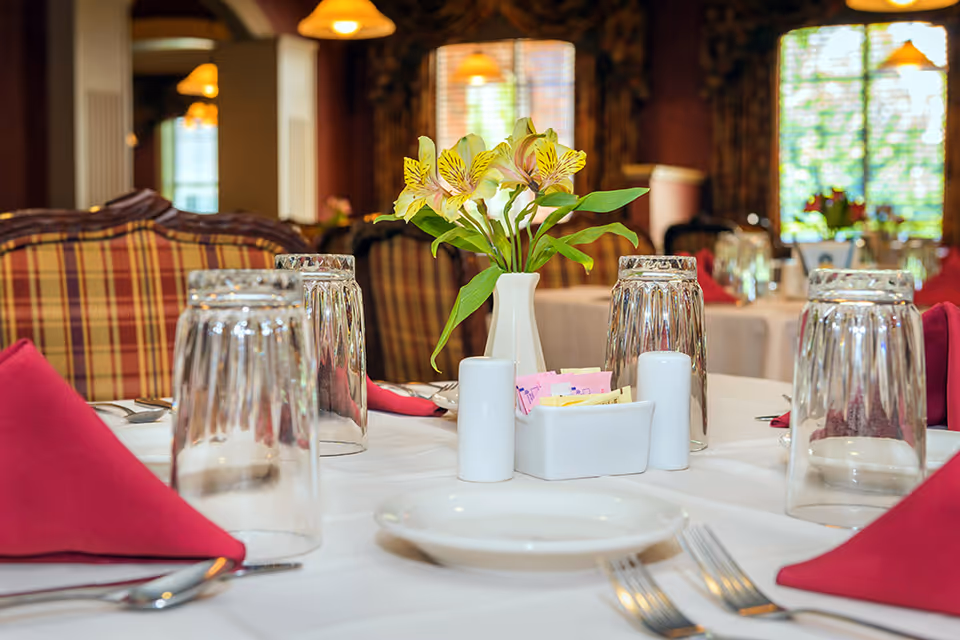 A dining table set with upside-down glasses, folded red napkins, a small vase of yellow flowers and condiment holders in an elegant dining room.