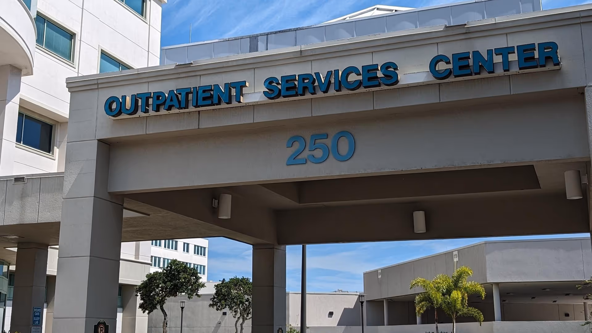Exterior view of a medical center entrance with a large 'OUTPATIENT SERVICES CENTER' sign.