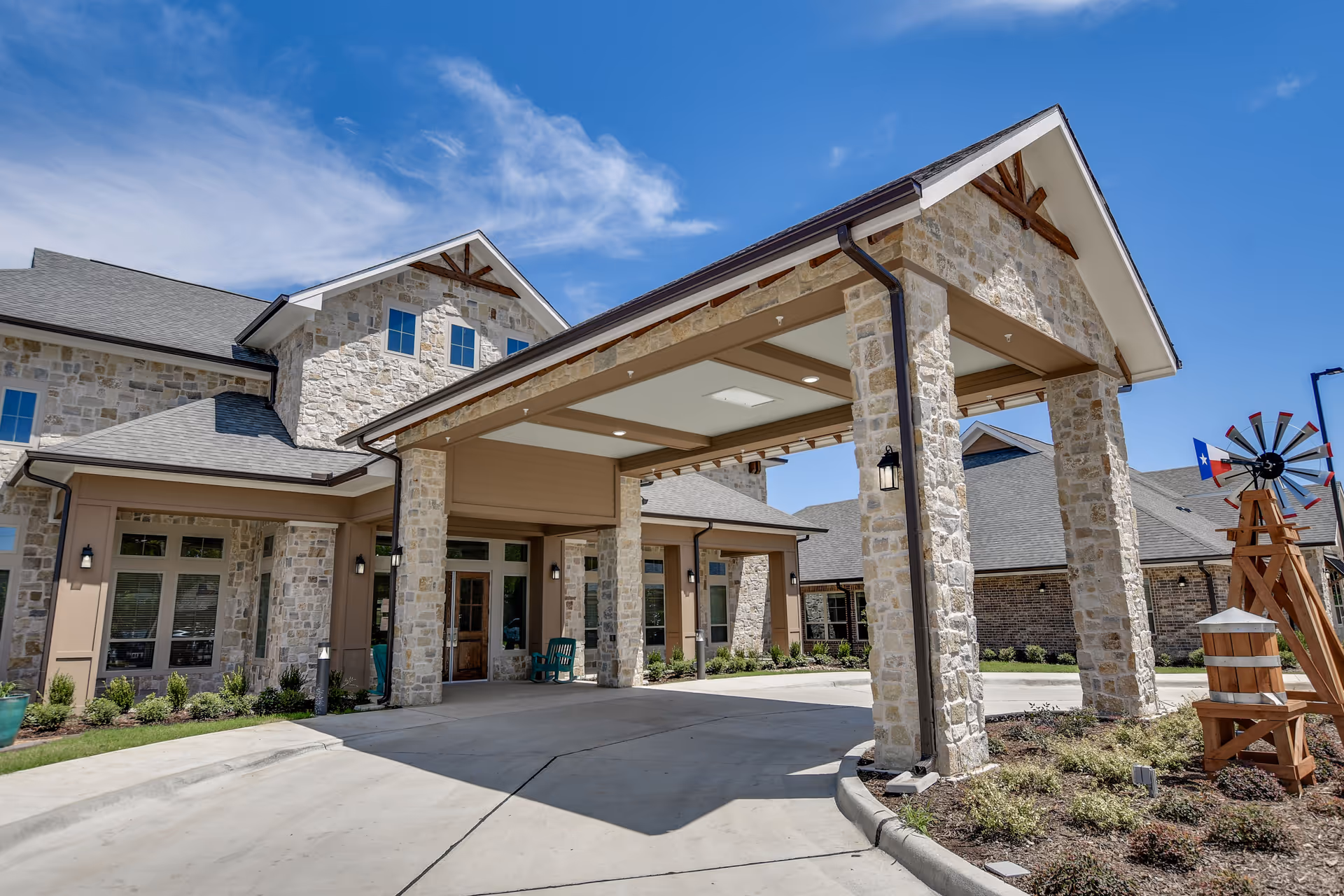Stone-clad building entrance with a covered porte-cochere over a circular driveway and a decorative windmill to the side.