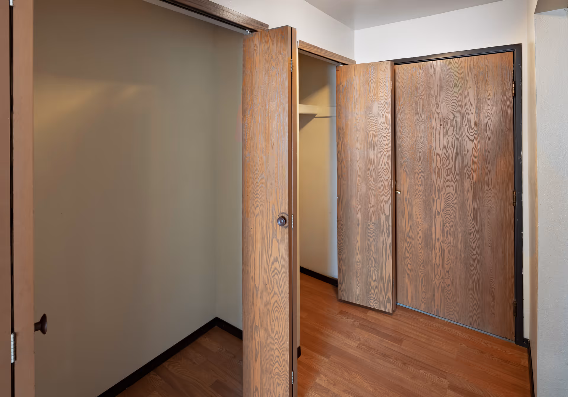 Open wooden closet doors revealing an empty closet and hardwood floor in a room