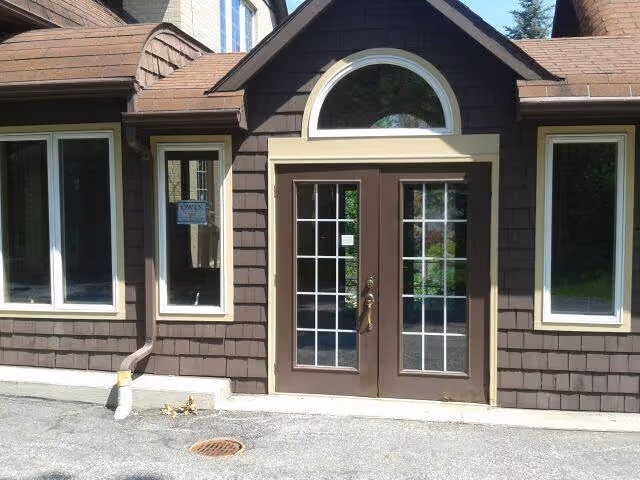 Front view of a brown shingled building with double glass doors and arched window