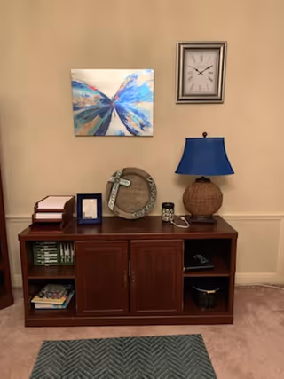Wooden sideboard with blue lamp, clock, artwork, and decorative items against beige wall.