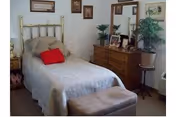 A cozy bedroom with a brass bed, dresser, mirror, plants, bench, and soft lighting.