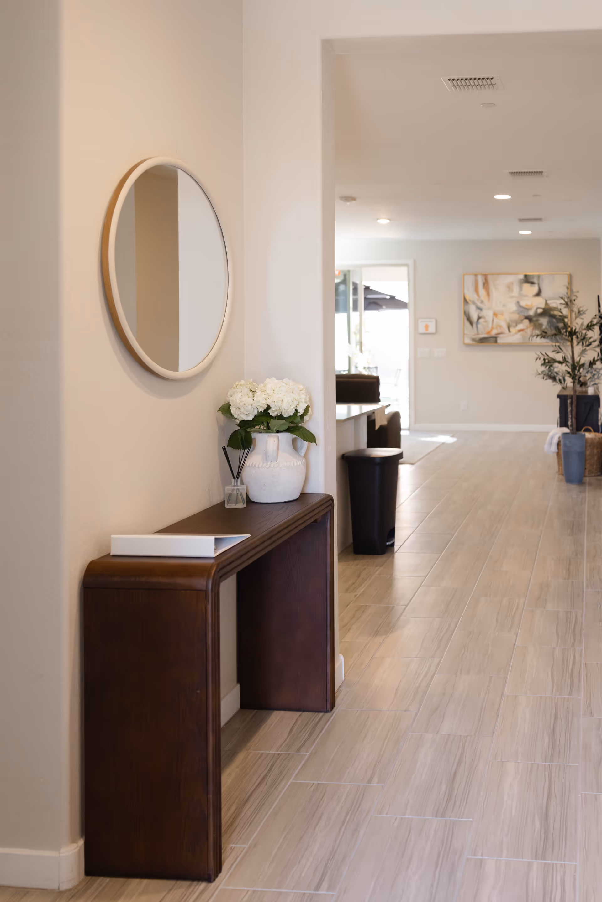A modern interior hallway with a circular mirror, console table, and flowers.