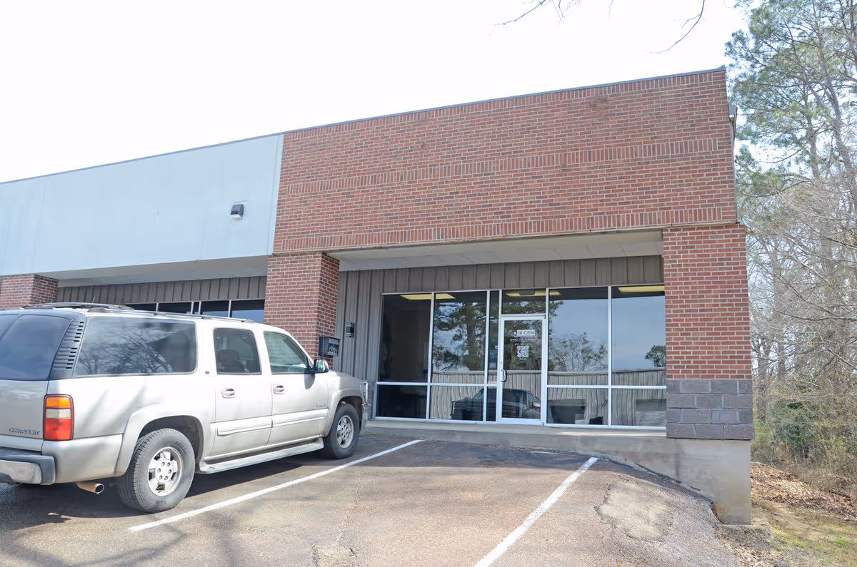 Exterior view of a brick building entrance with glass doors and a parked SUV