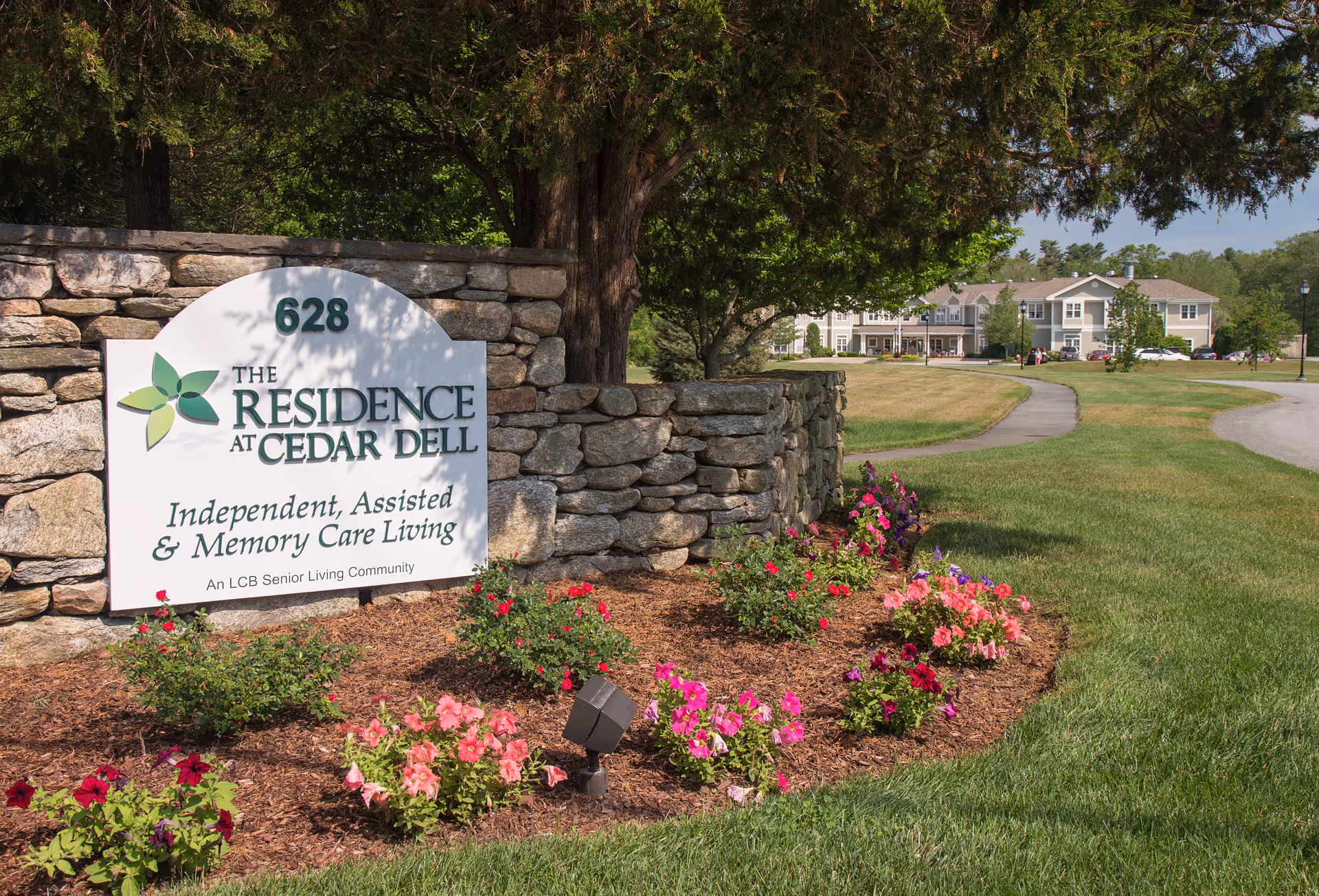 The Residence at Cedar Dell sign on a stone wall with blooming flowers and lawn