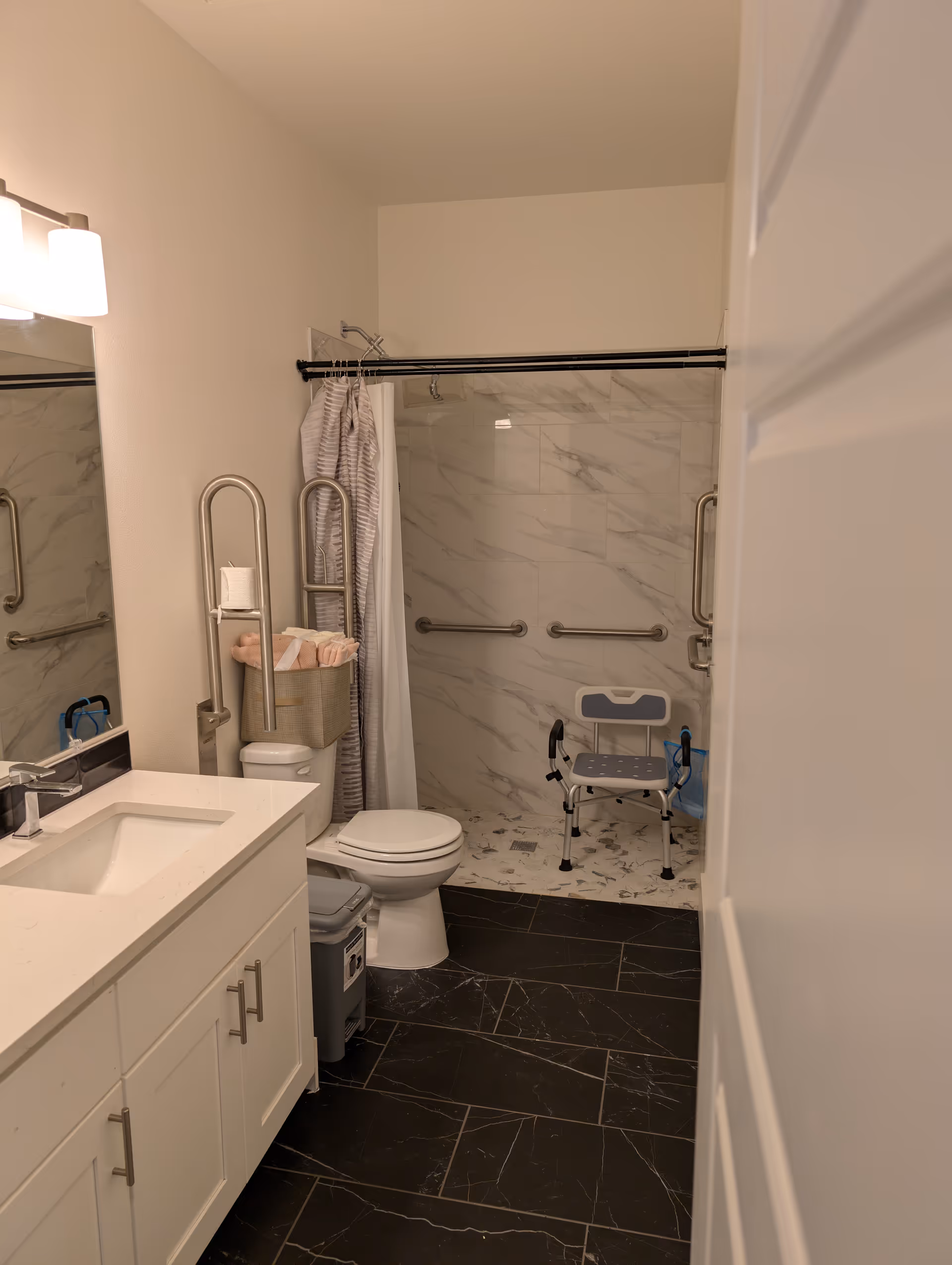 Accessible bathroom with shower chair, grab bars, sink, and toilet.