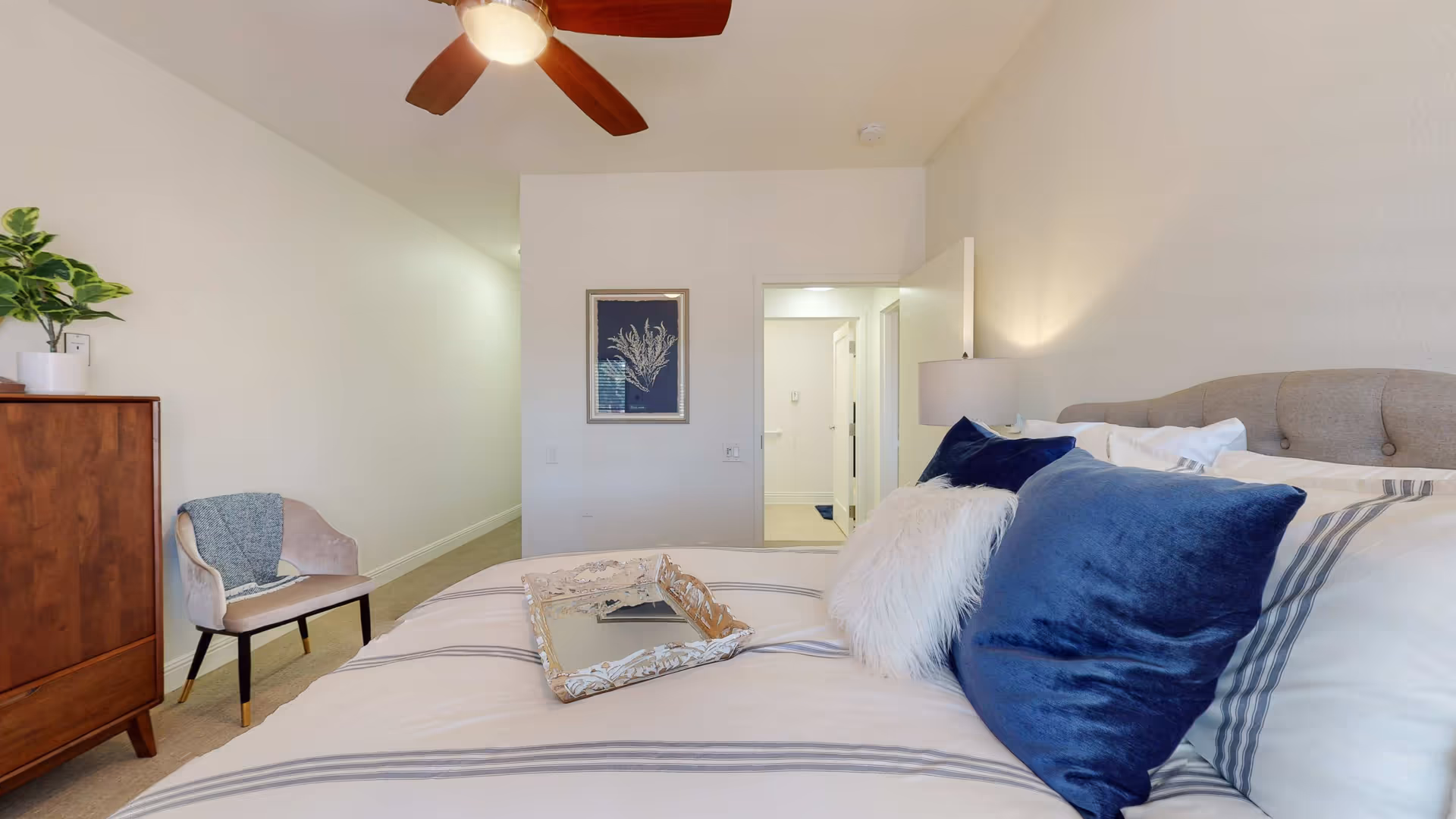 Bright bedroom featuring a bed, dresser, chair, and ceiling fan.